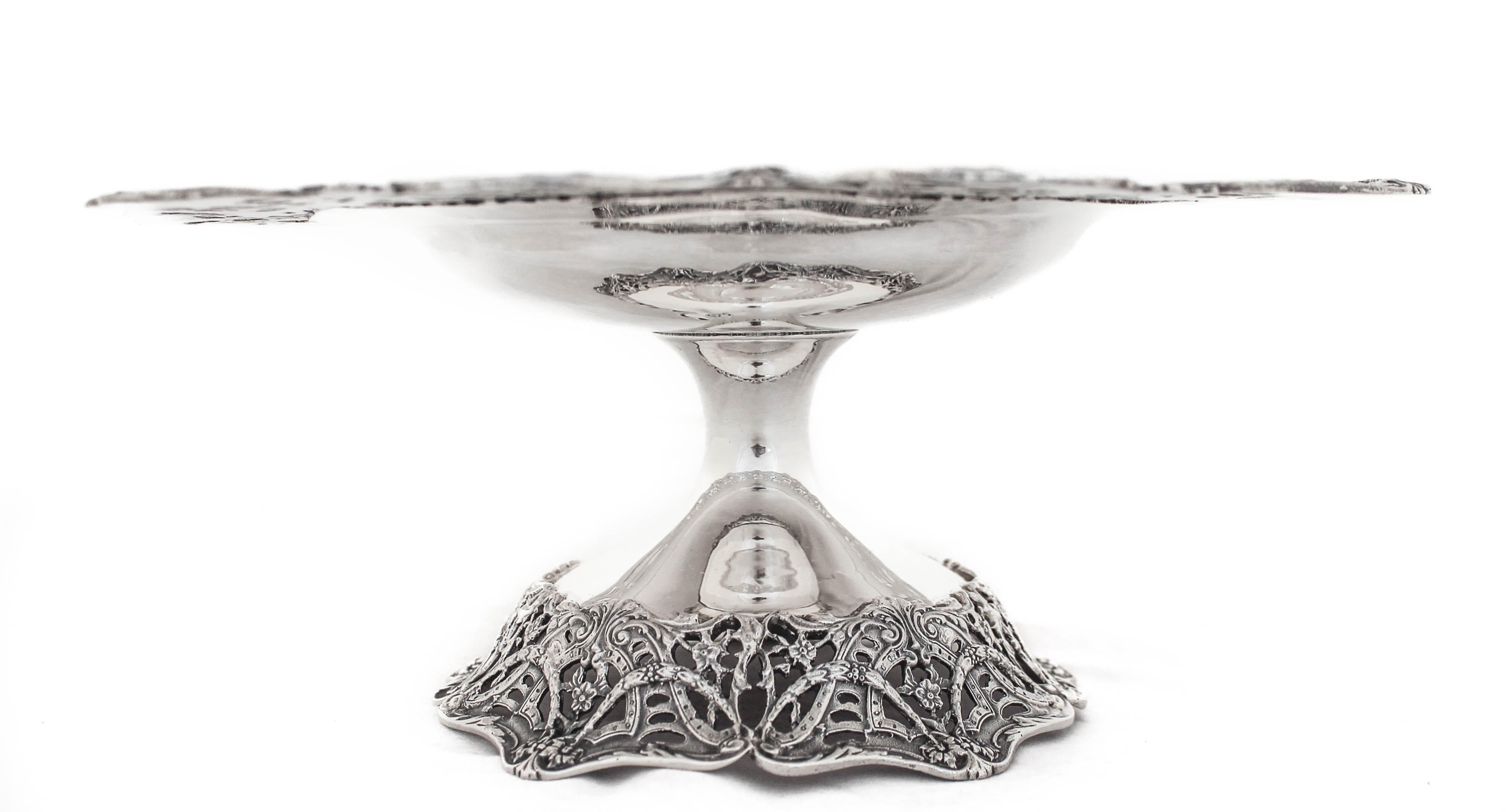 Being offered is a large sterling silver tazza.  It has an old-world pattern going around the scalloped edge and base.  Wreaths, flowers and bows come together in an elaborate feast for the eyes.  The center is curved; more of a bowl than a flat