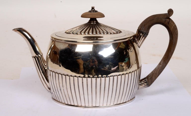 Sterling silver tea pot by William Plummer, London, circa 1797. The oval shape has half reeded, fluted decoration on the body, top and curved spout. The lid with an ‘invisible’ hinge is topped by a oval wooden and sterling silver finial. The tea pot