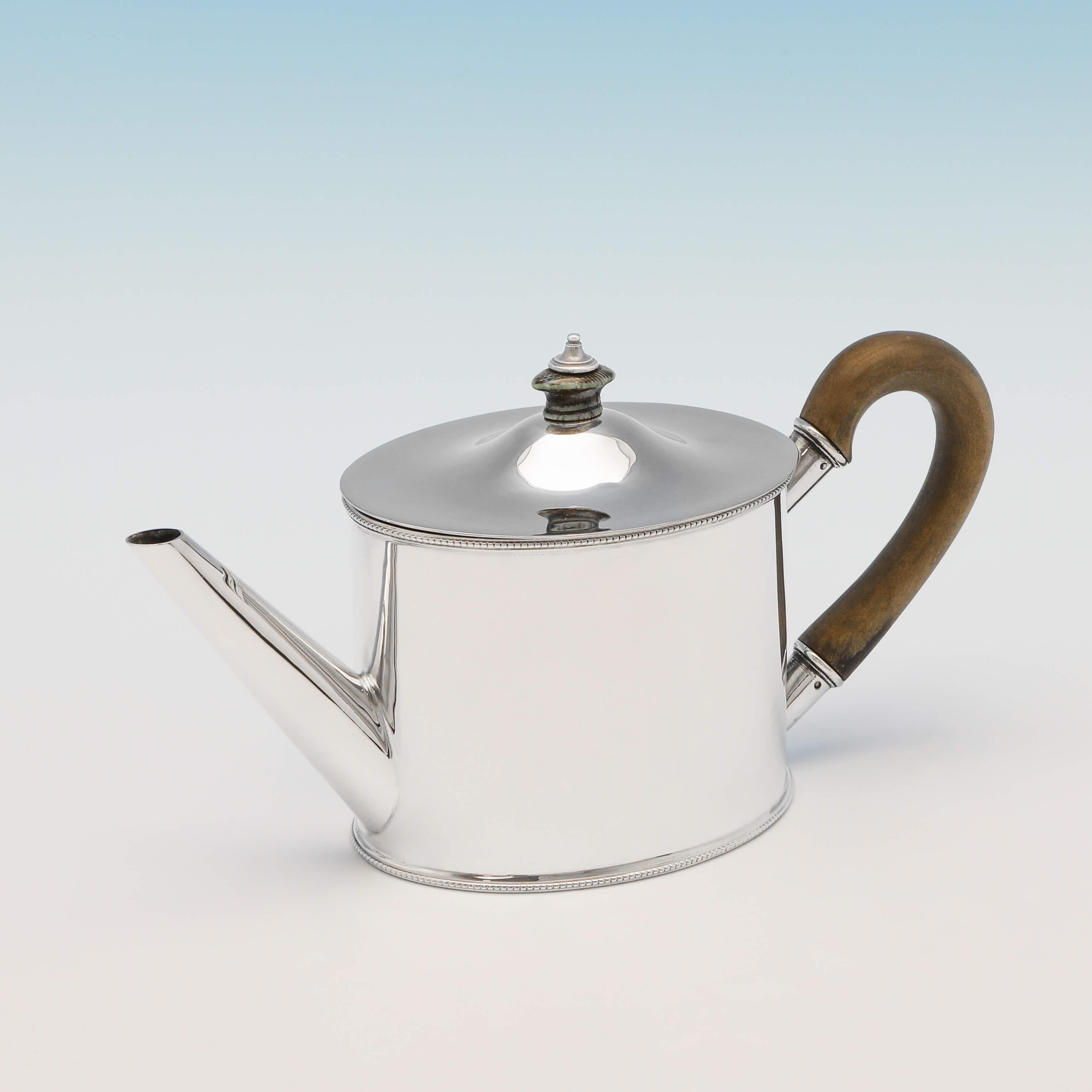Hallmarked in Sheffield in 1924 by Roberts & Belk, this handsome, sterling silver teapot, is plain in style, with bead borders, a wooden handle, and a removable lid. The teapot measures 8.5