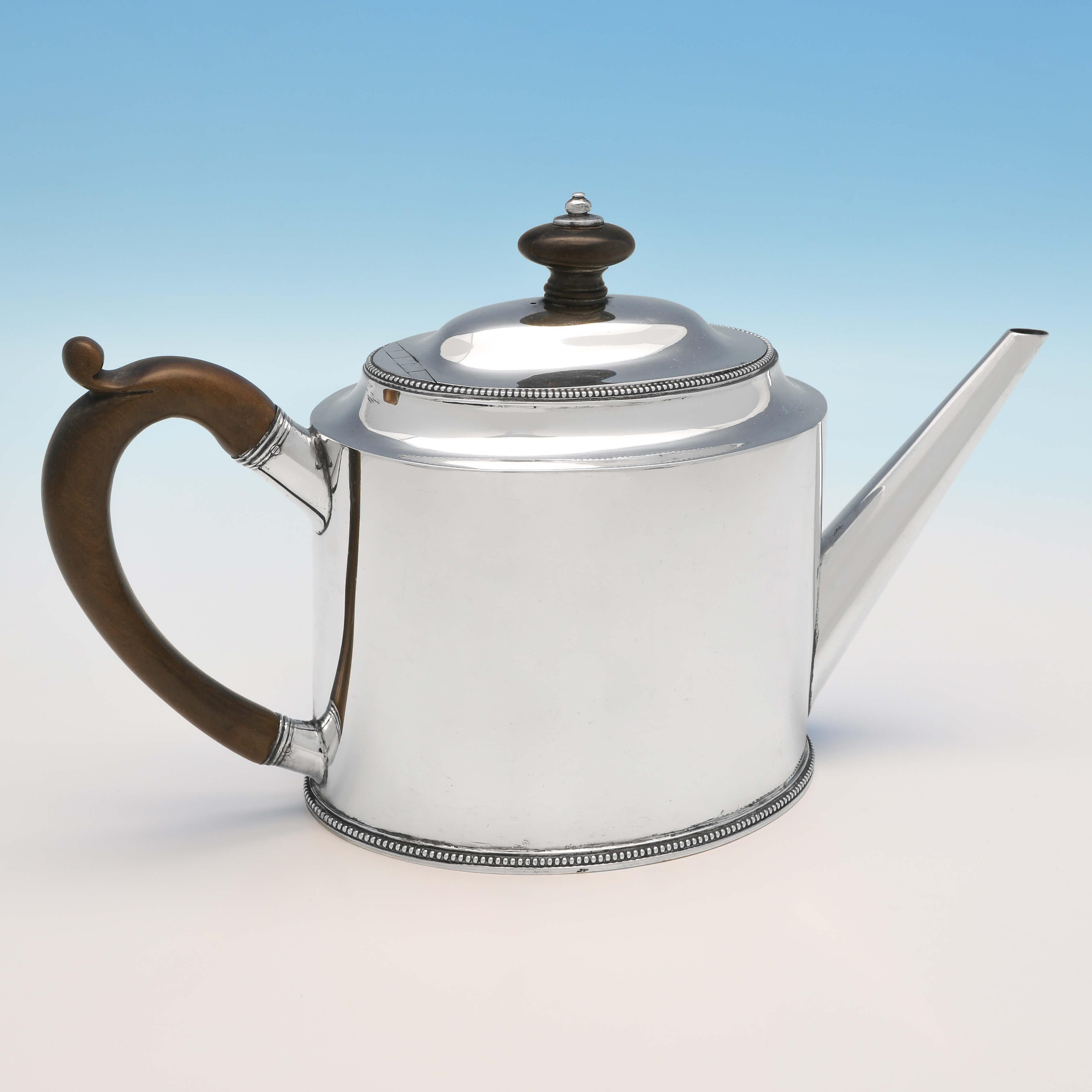 Hallmarked in London in 1785 by Hester Bateman, this elegant, George III, antique sterling silver teapot and stand, is plain in style, embellished with fine beading, and features a wooden handle and finial. The teapot on stand measures 7