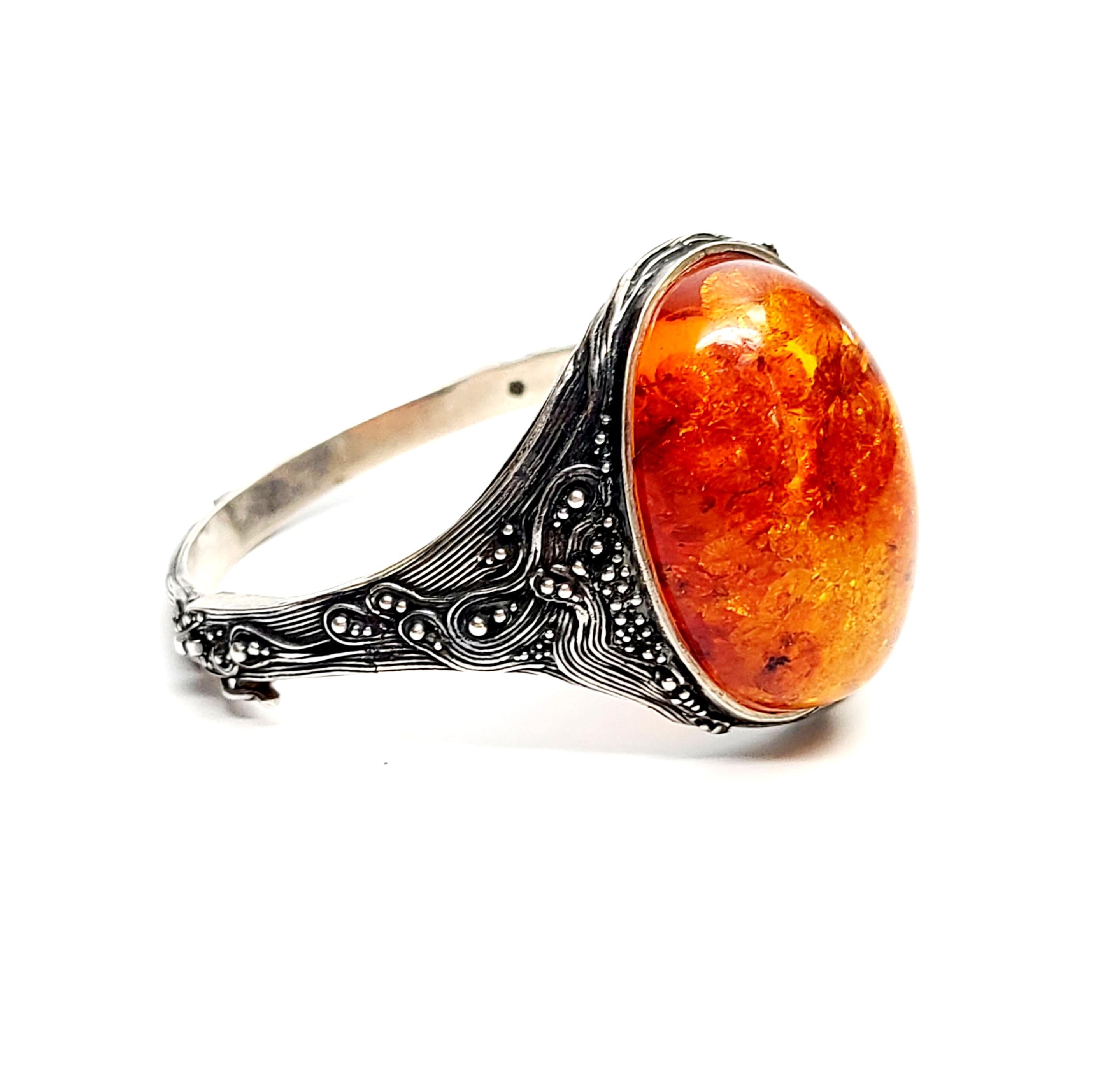 Vintage silver textured hinged bangle bracelet with large oval amber stone.

This bracelet is a beautiful example of textured metalwork. Large oval shaped amber stone bezel set in front. An inconspicuous slide closure with safety clasp allows the