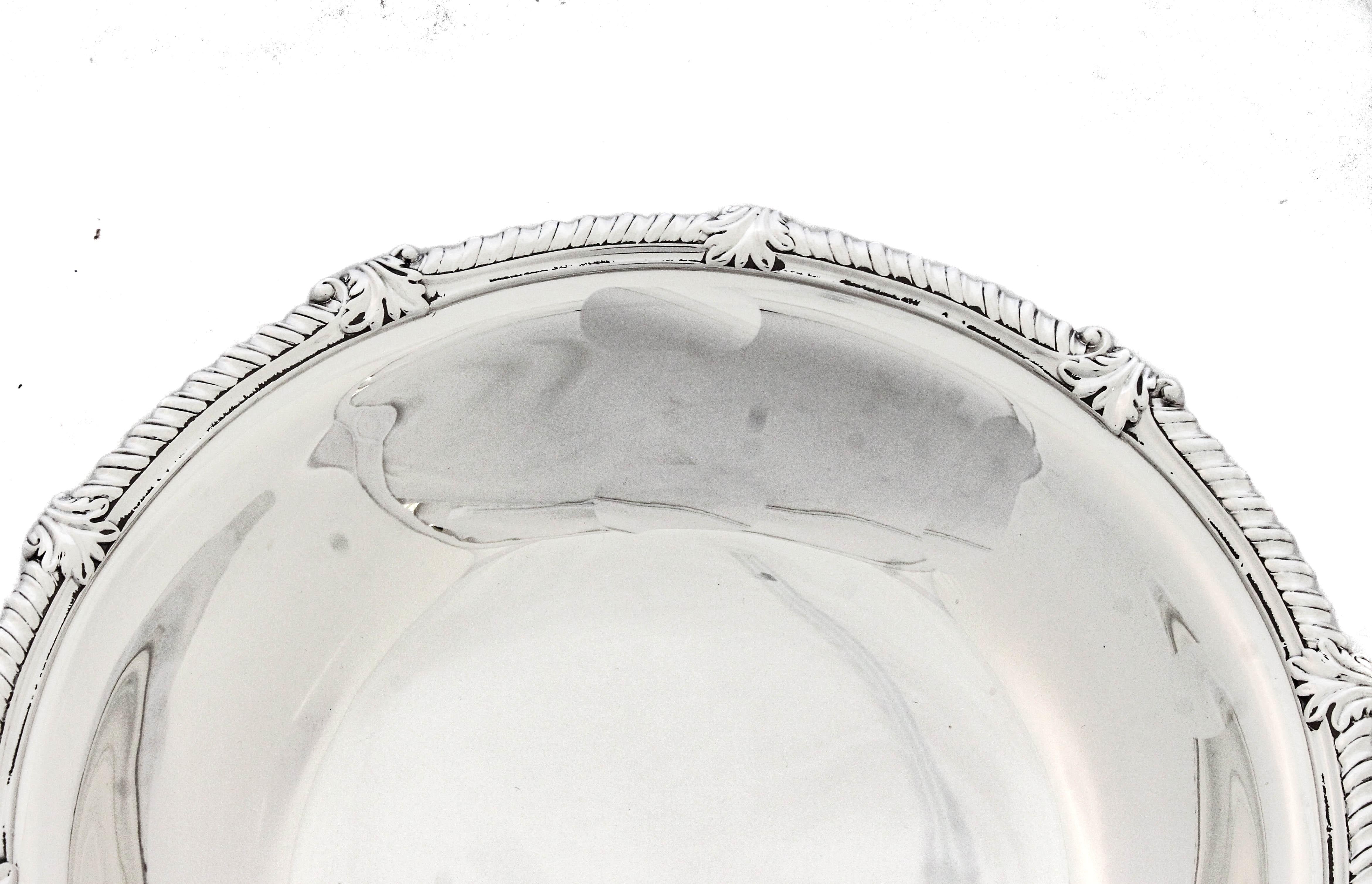 Se ofrece un cuenco de plata de ley de Tiffany and Company.  El cuenco está sobre un pedestal, por lo que se apoya sobre la superficie.  Tiene un ribete en forma de gota alrededor del borde intercalado con un diseño de hojas.  Es un cuenco de buen