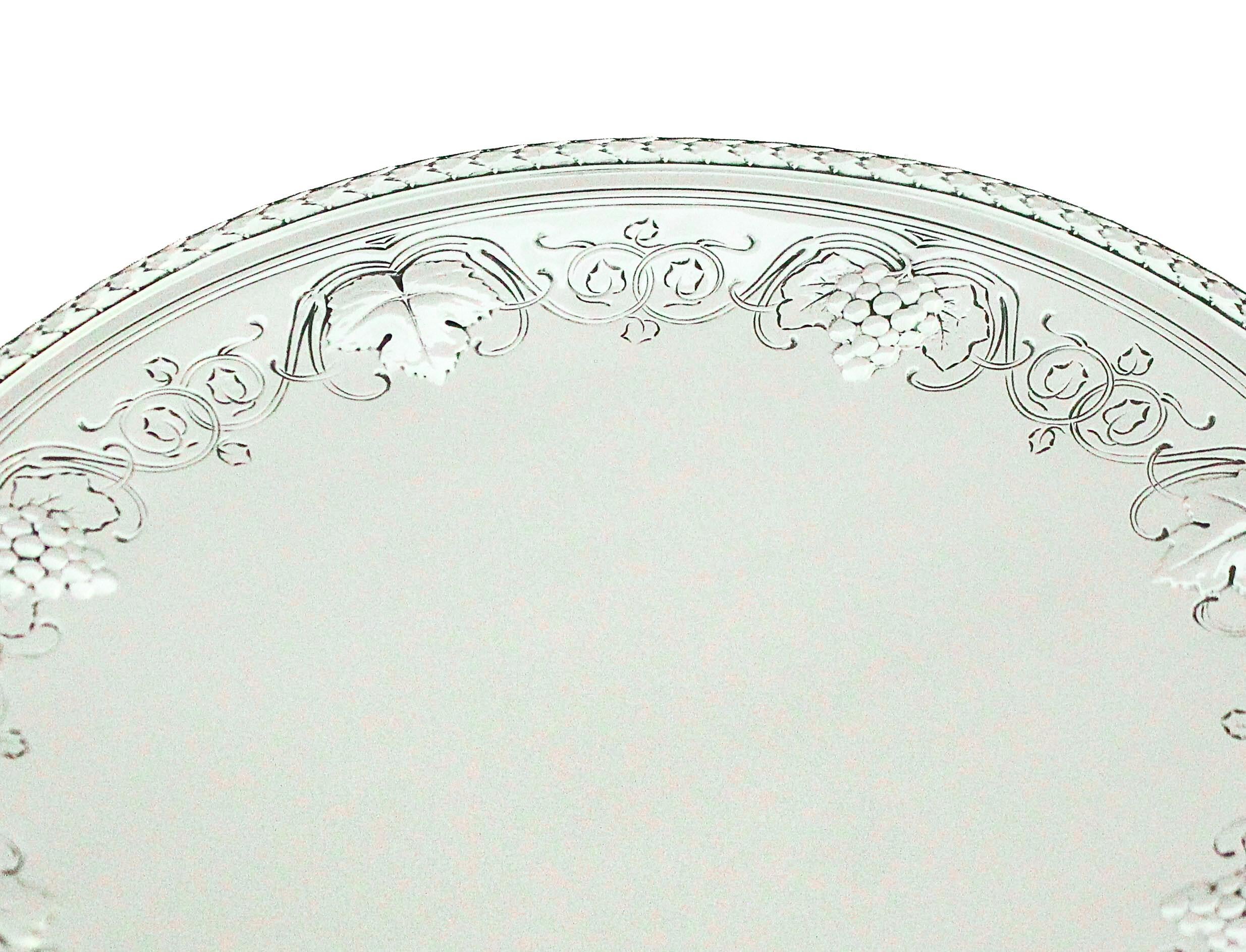 Un elegante vassoio rotondo in argento sterling, realizzato in un raffinato stile classico e sollevato su un basso piedistallo circolare. L'elevazione fornisce sia stabilità che un sottile senso di prominenza, dando al vassoio una presenza