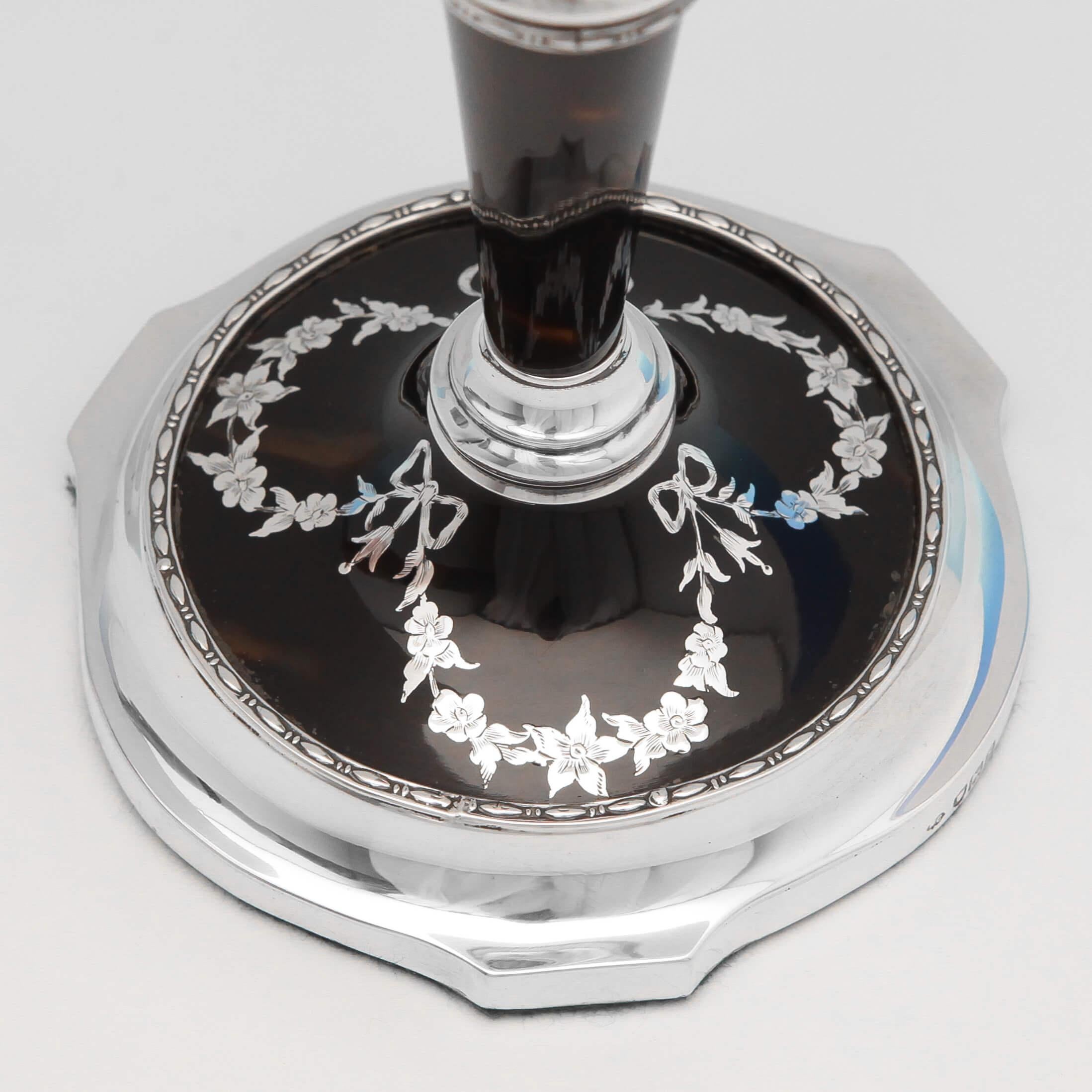 Hallmarked in London in 1913 by William Comyns, this attractive pair of sterling silver candlesticks, feature tapered tortoiseshell columns and tortoiseshell bases with inlaid silver bows and garlands. Each candlestick measures 7