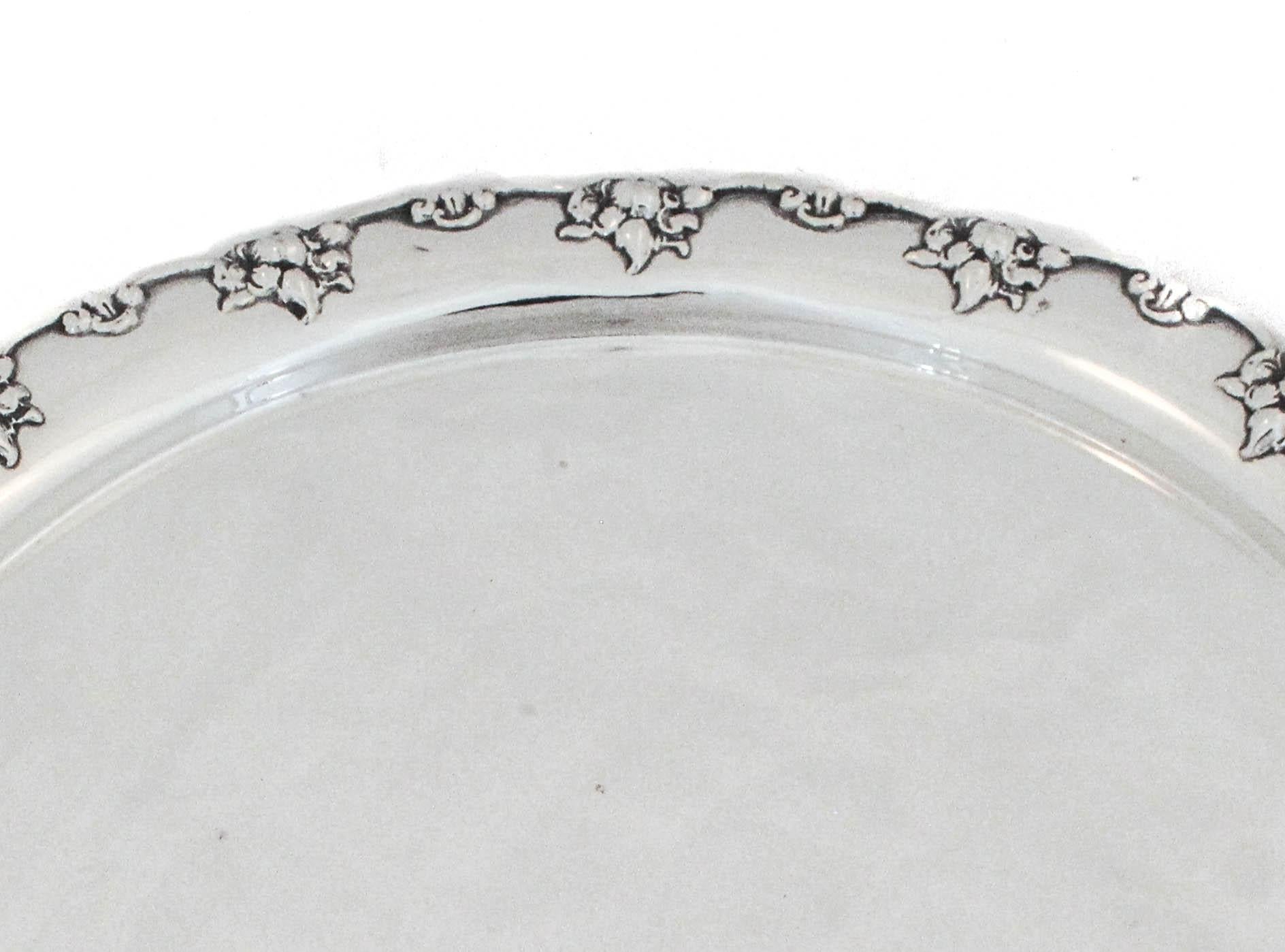 Estamos encantados de ofrecer esta bandeja de plata de ley fabricada por Gorham Silversmiths de Providence, Rhode Island, hacia 1880.  Esta pieza antigua de ciento cuarenta y cinco años tiene un borde festoneado con racimos de flores alrededor.  Es
