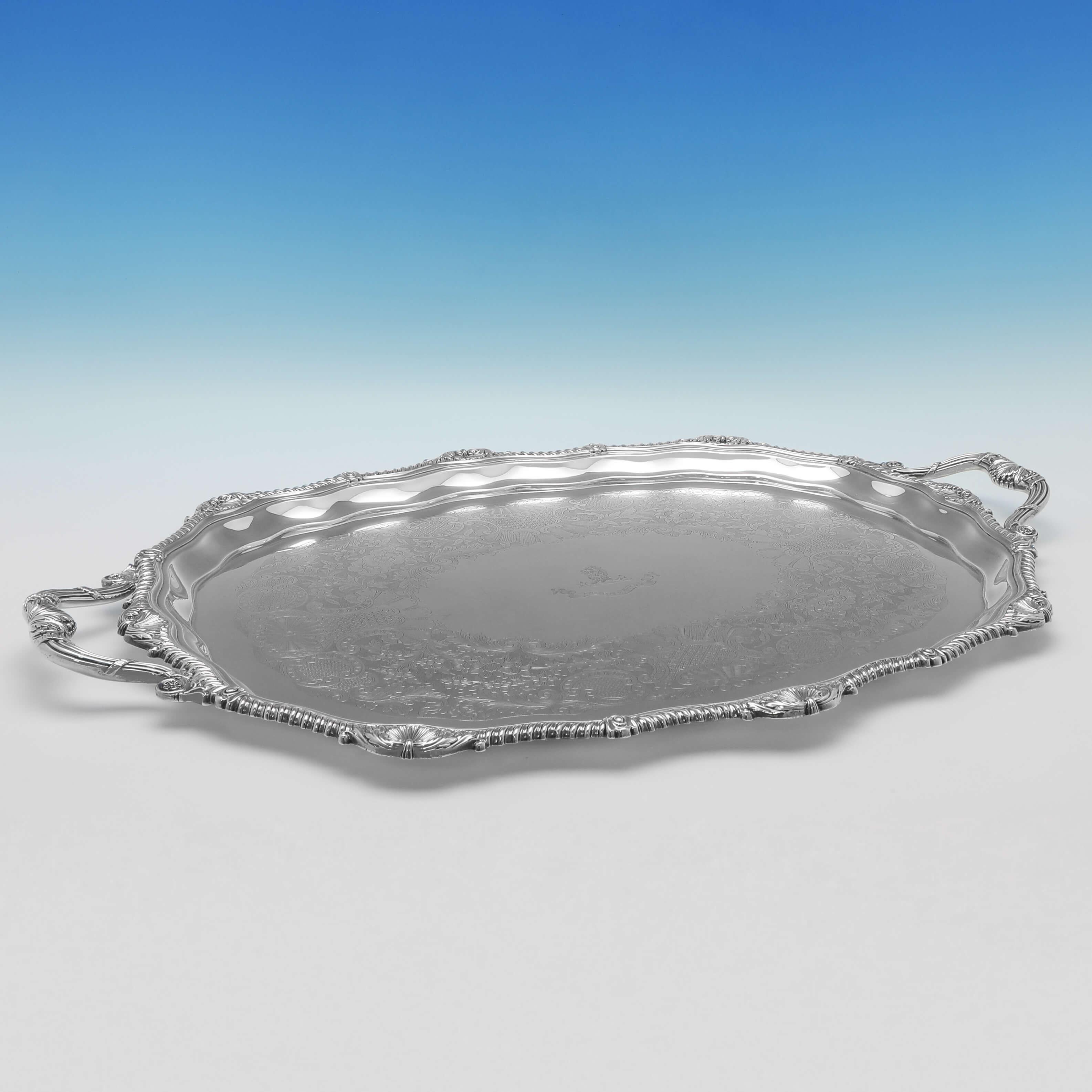 Hallmarked in London in 1905 by Hawksworth Eyres & Co, this heavy, Edwardian, antique Sterling Silver Tray, features flat chased floral and scroll decoration to the body with a shaped shell and gadroon border, and an engraved crest and motto to the