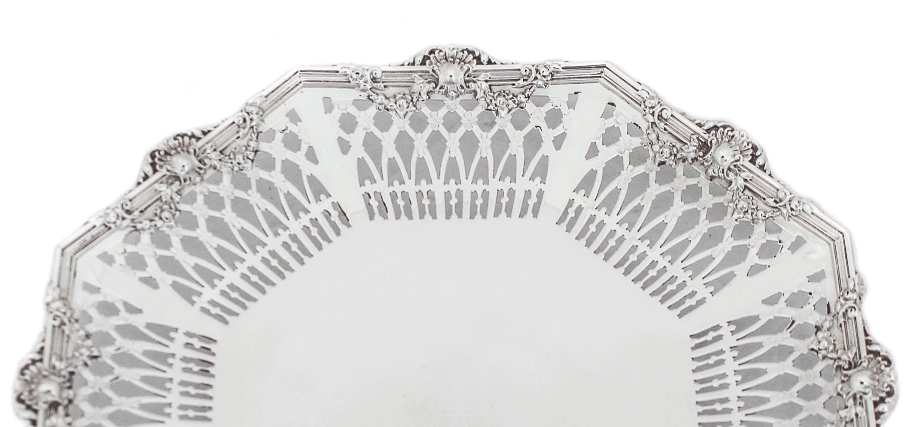 This beautiful sterling silver tray has a reticulated border and a fluted rim. It has a pedestal so it’s propped off the surface. It is an octagon shaped tray with wreaths and floral motifs around the sides. A piece of old-world workmanship at its