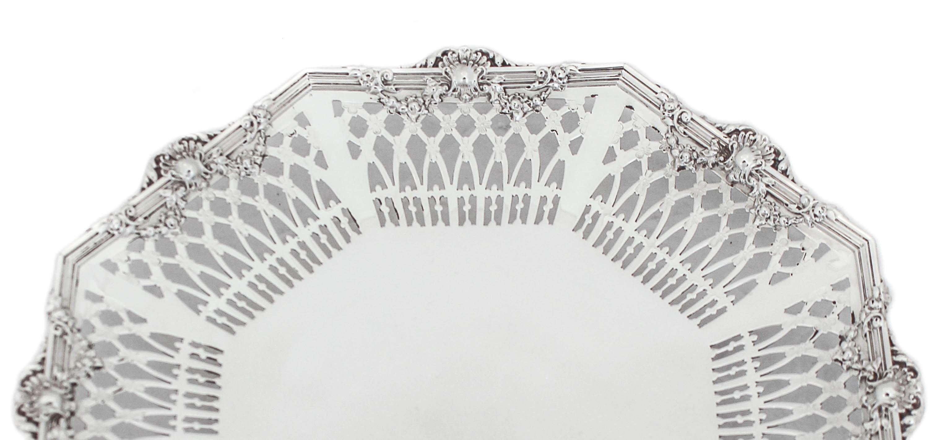 Esta hermosa bandeja de plata de ley tiene un borde reticulado y un reborde estriado. Tiene un pedestal para que se apoye sobre la superficie. Es una bandeja de forma octogonal con coronas y motivos florales alrededor de los lados. Una pieza de