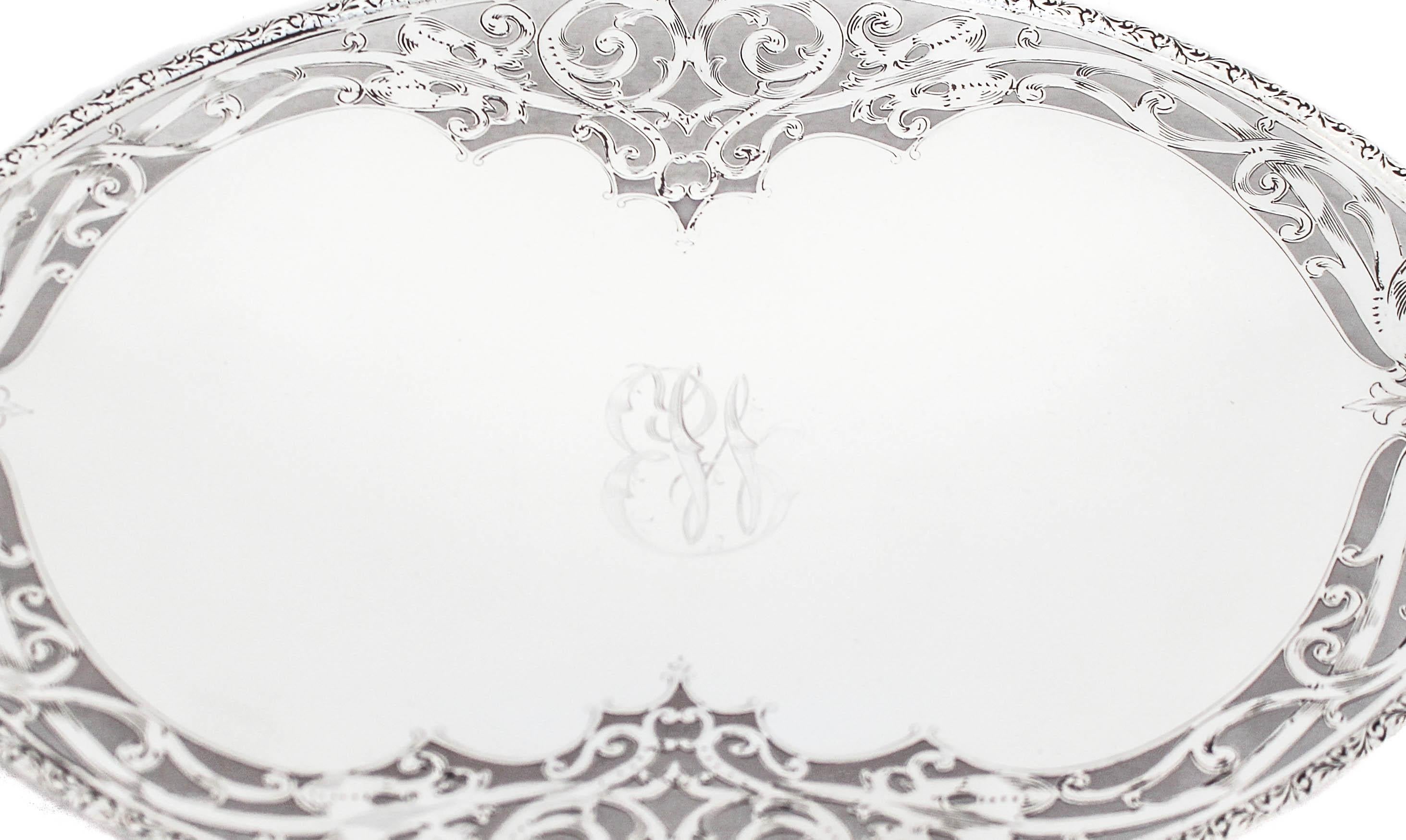 Se ofrece una hermosa bandeja de plata de ley con un elegante diseño reticulado que rodea el borde.  Es una pieza ovalada con asas a cada lado y se alza sobre un pedestal.  Todo el borde tiene un motivo recortado Art Nouveau que complementa las asas