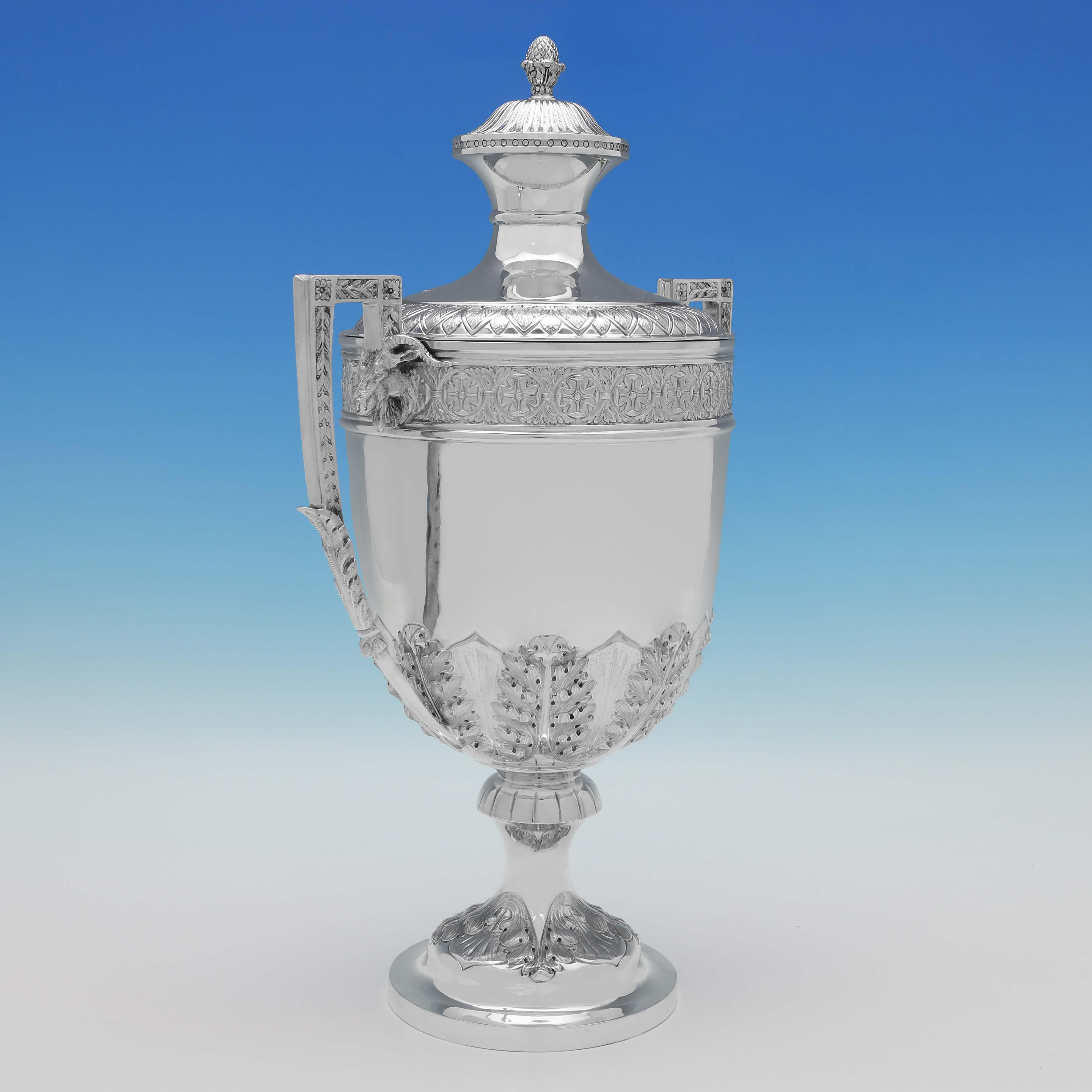 Hallmarked in Sheffield in 1902 by Mappin & Webb, this striking, Edwardian, Antique Sterling Silver Trophy Cup & Cover, is in the Neoclassical Revival taste, featuring a pineapple finial, chased anthemion leaves around the body, and rams head masks