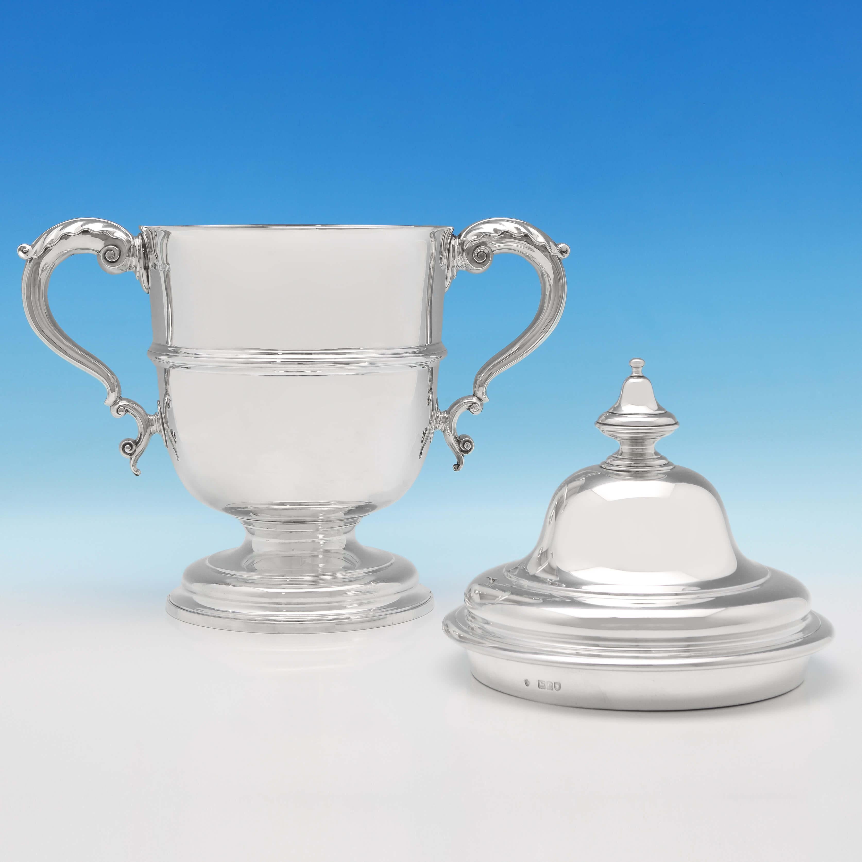 Hallmarked in London in 1903 by Edward Barnard & Sons, this large, Edwardian, antique, sterling silver trophy, features acanthus detailed scroll handles, a central reed band and a pedestal foot. The trophy measures 16
