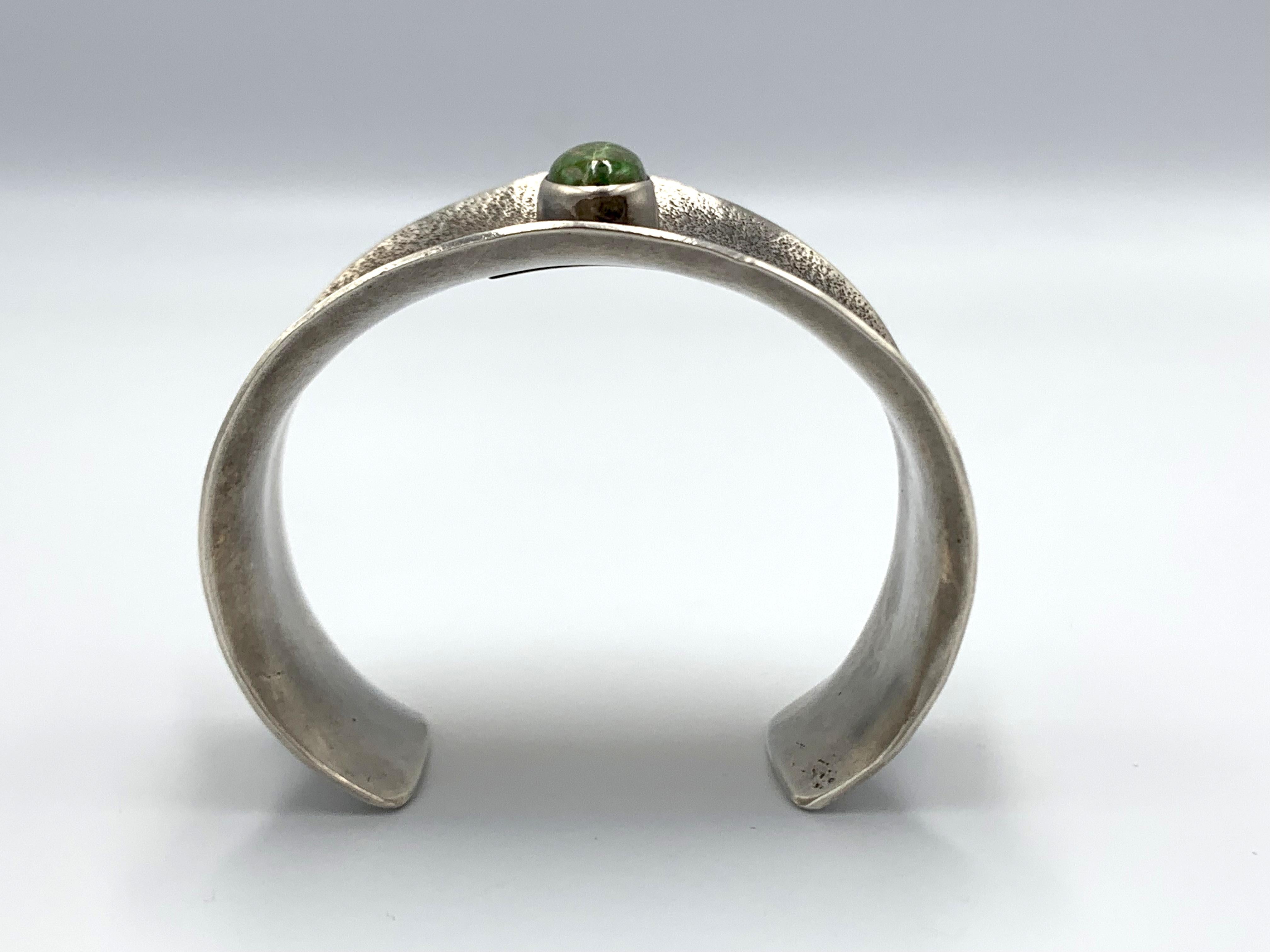 Questo bracciale largo e concavo in argento sterling è stato realizzato a mano dall'argentiere Navajo Julian Chavez con la tradizionale tecnica della fusione in tufo. Il bracciale presenta una raffinata stampa a mano e una pietra ovale di turchese