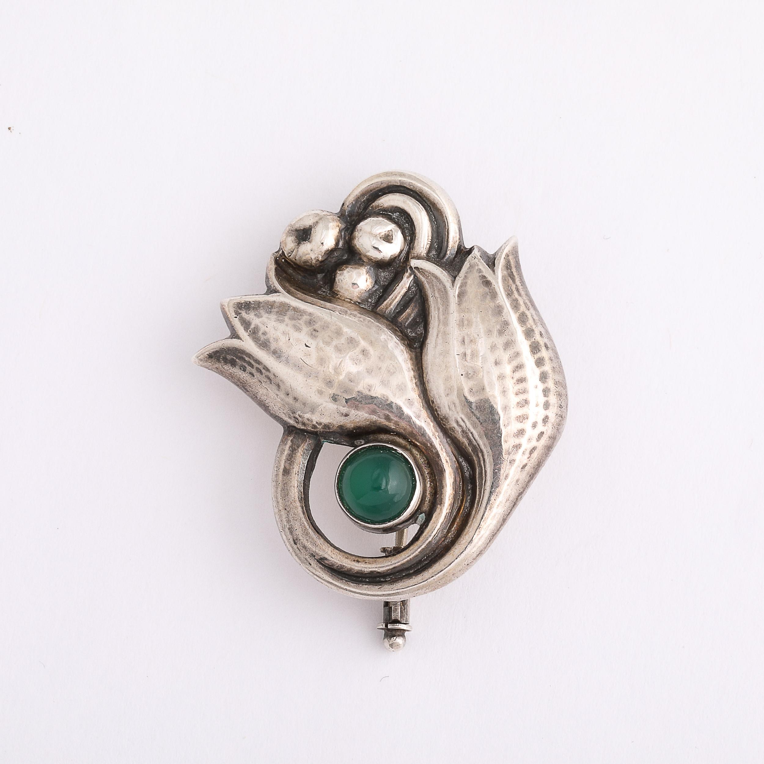 This highly elegant Aesthetic movement Sterling Silver Tulip Form Brooch W/Emerald Cabachon by Georg Jensen originates from Denmark, Circa 1910. This piece catches the eye with a strikingly colored cabachon emerald surrounded by the beautiful tulips