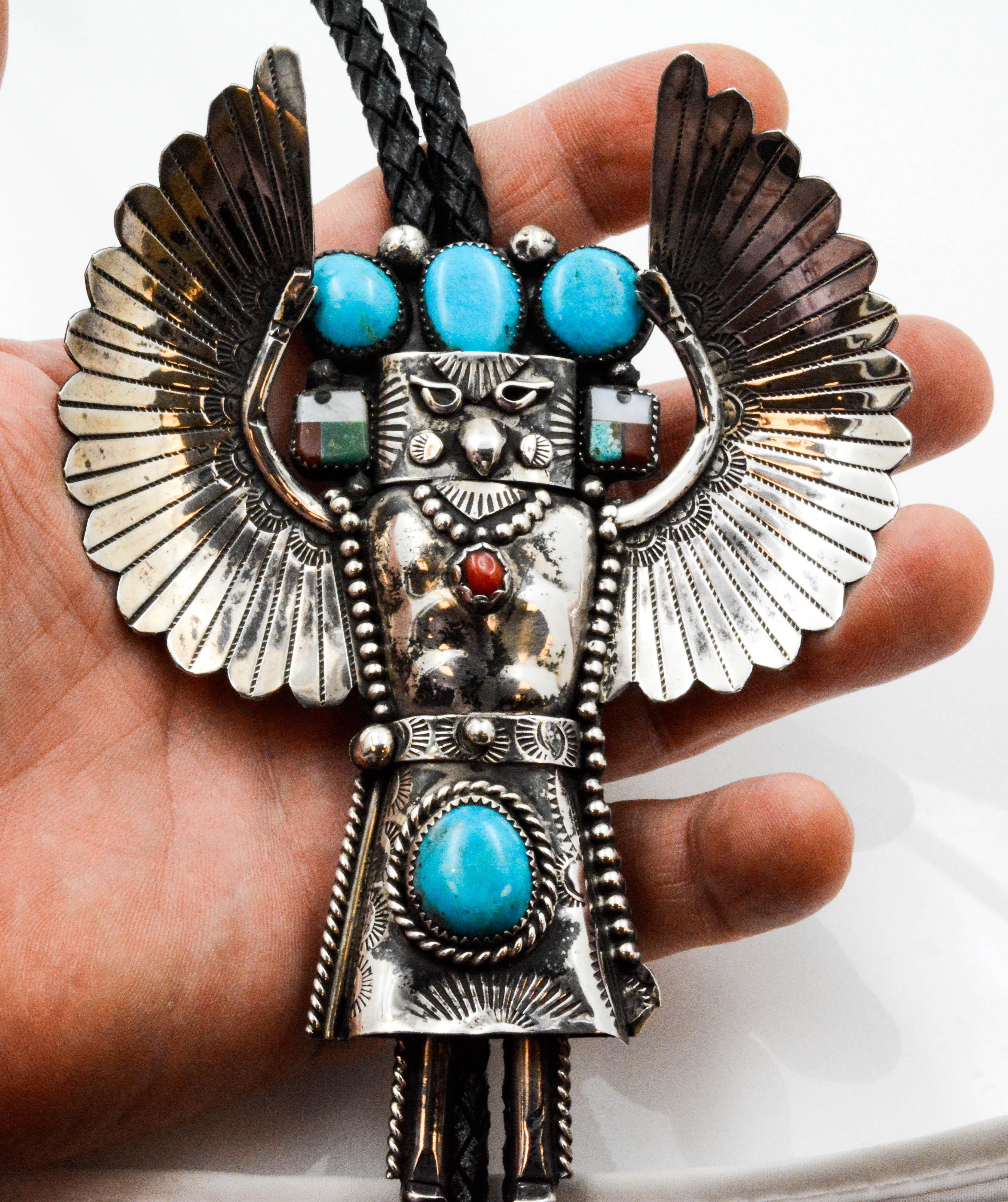Circa 1970's handcrafted Sterling Silver Eagle Kachina Bolo tie set with 4 oval Turquoise stones. An oval Coral stone is bezel set on the chest of the Eagle Kachina, and Mother of Pearl is bezel set at the ears. This is an impressive piece with