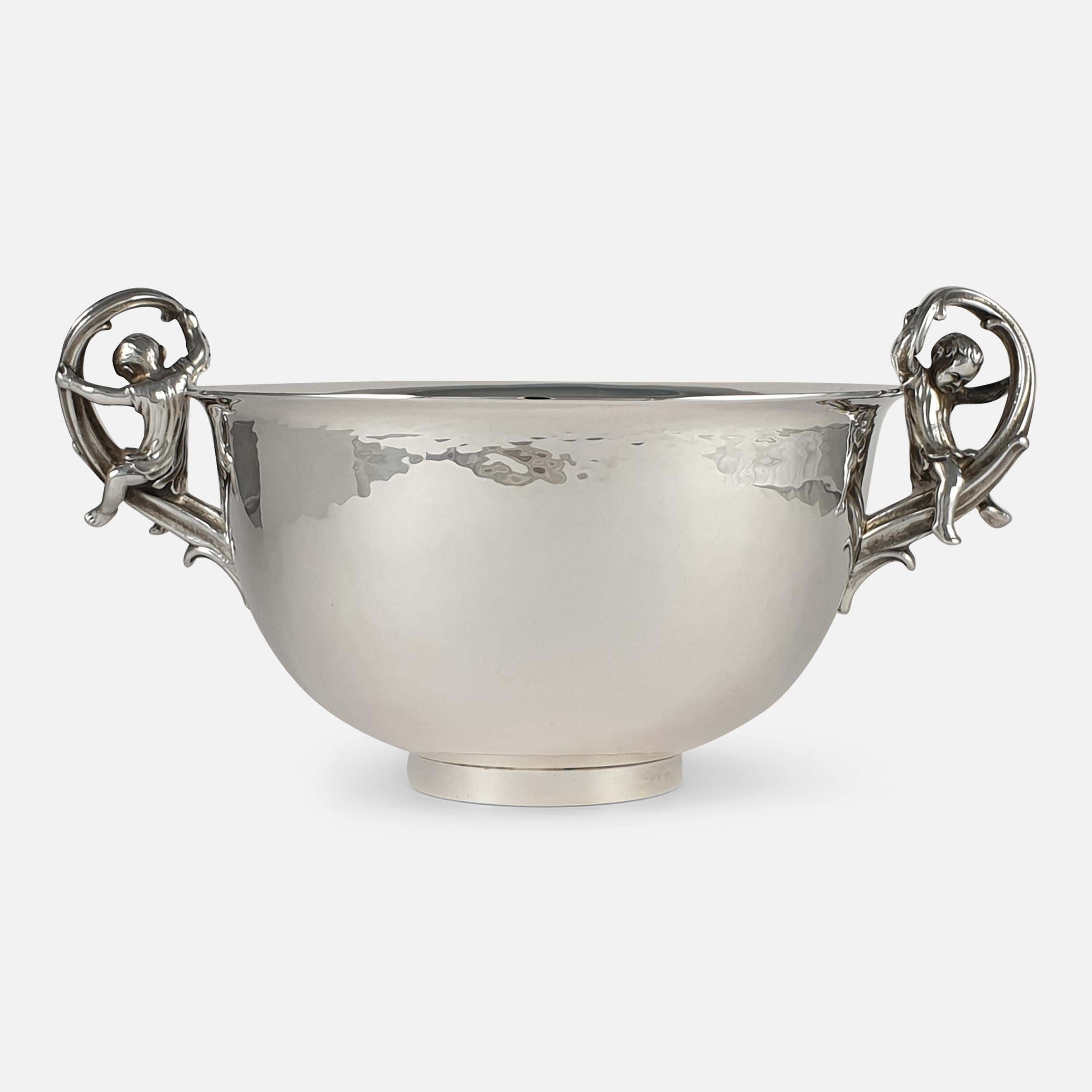A sterling silver bowl by Leslie G. Durbin, featuring twin scroll handles adorned with figures of children, one depicted with a splint. The bowl is crafted with spot-hammered decoration and is supported by a circular foot.

• Assay: .925 Sterling