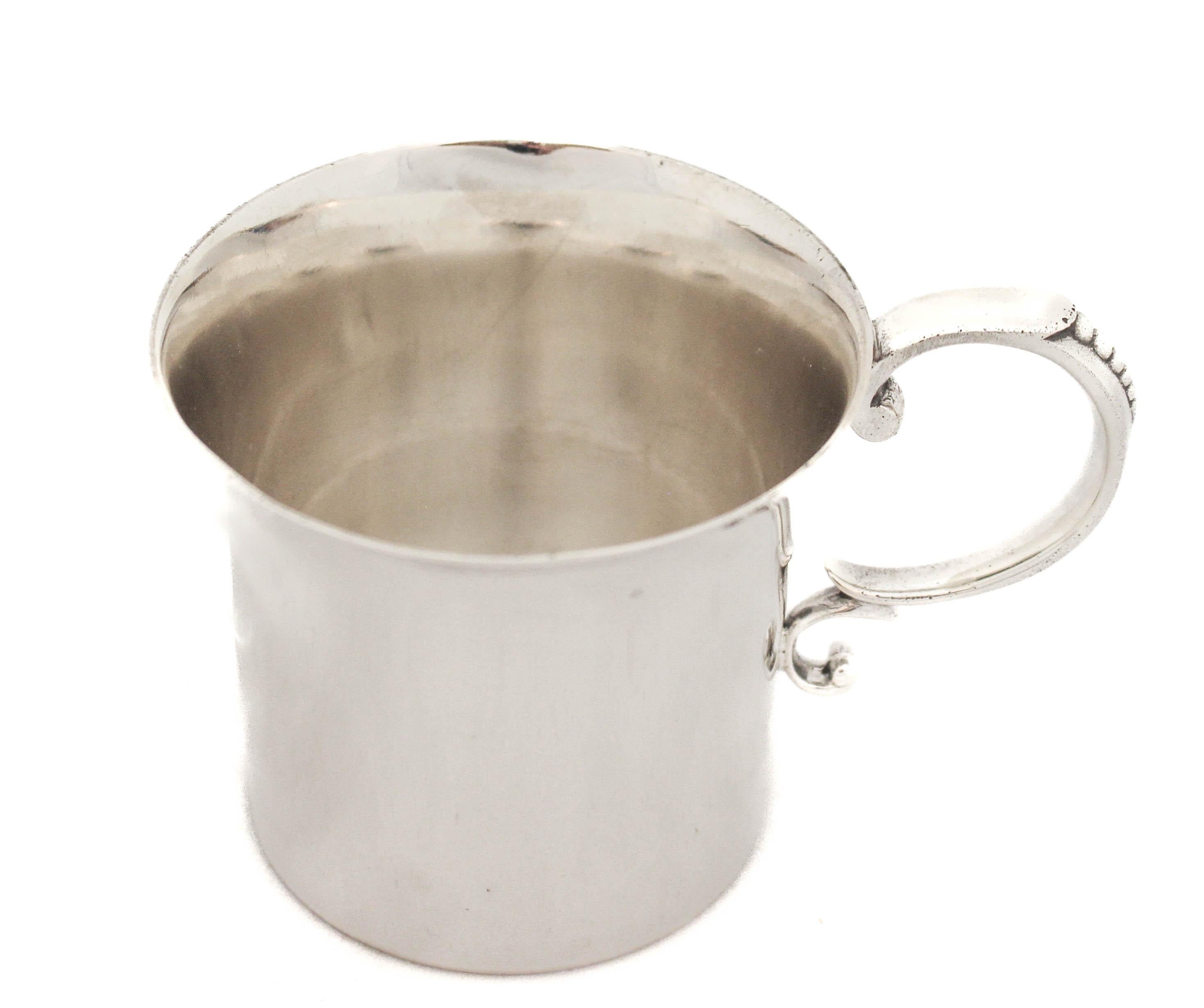 Being offered is a sterling silver baby cup by the Watson Silver Company.  It has a minimalist design based on a Federalist silver pattern from 1700 by John Coney.  The only ornamentation is on the handle; a row of six beads goes down the handle.  A
