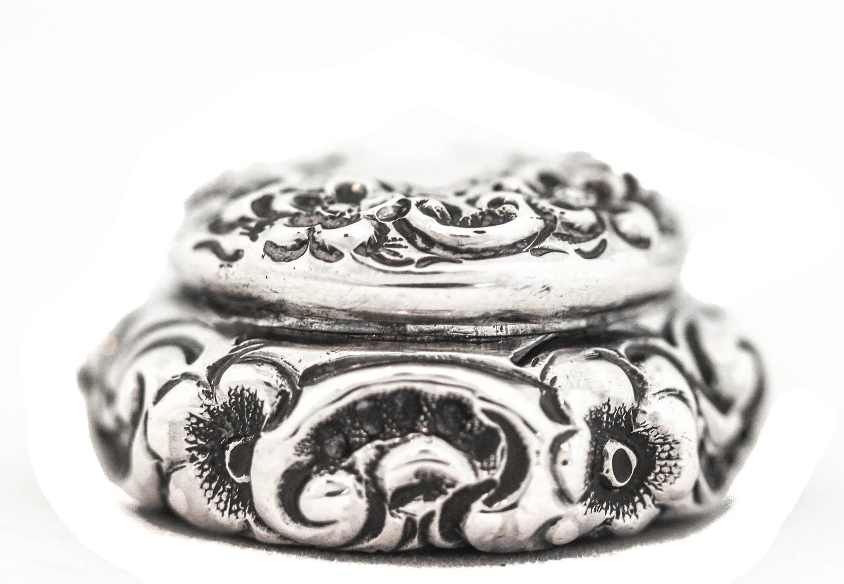 Angeboten wird eine viktorianische Pillendose aus Sterlingsilber, hergestellt von La Pierre Silver.  Sie hat ein reich verziertes Äußeres mit einem Repousse-Stil aus geblasenen (erhabenen) Blumen - sowohl auf dem Korpus als auch auf dem Deckel.  Sie
