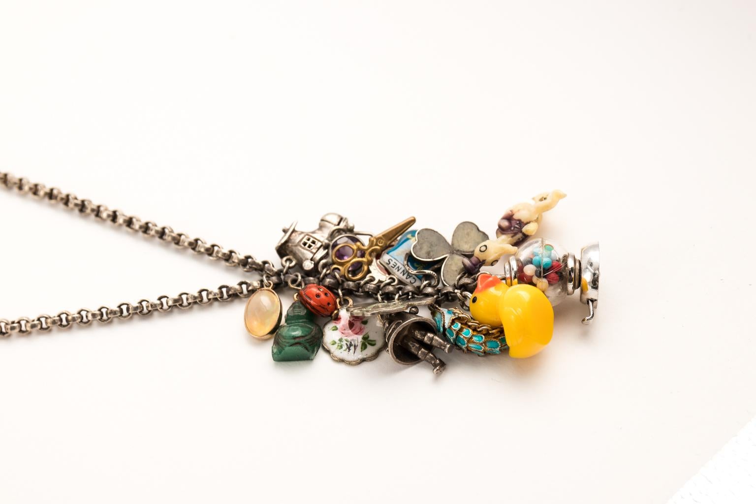 Sterling silver chain necklace with 18 vintage charms in a cluster that measures 15.75 Inch Long that features a sterling silver rolo chain with Enamel, Jade,Opal,Glass, Amethyst, Lucite, and Brass.
