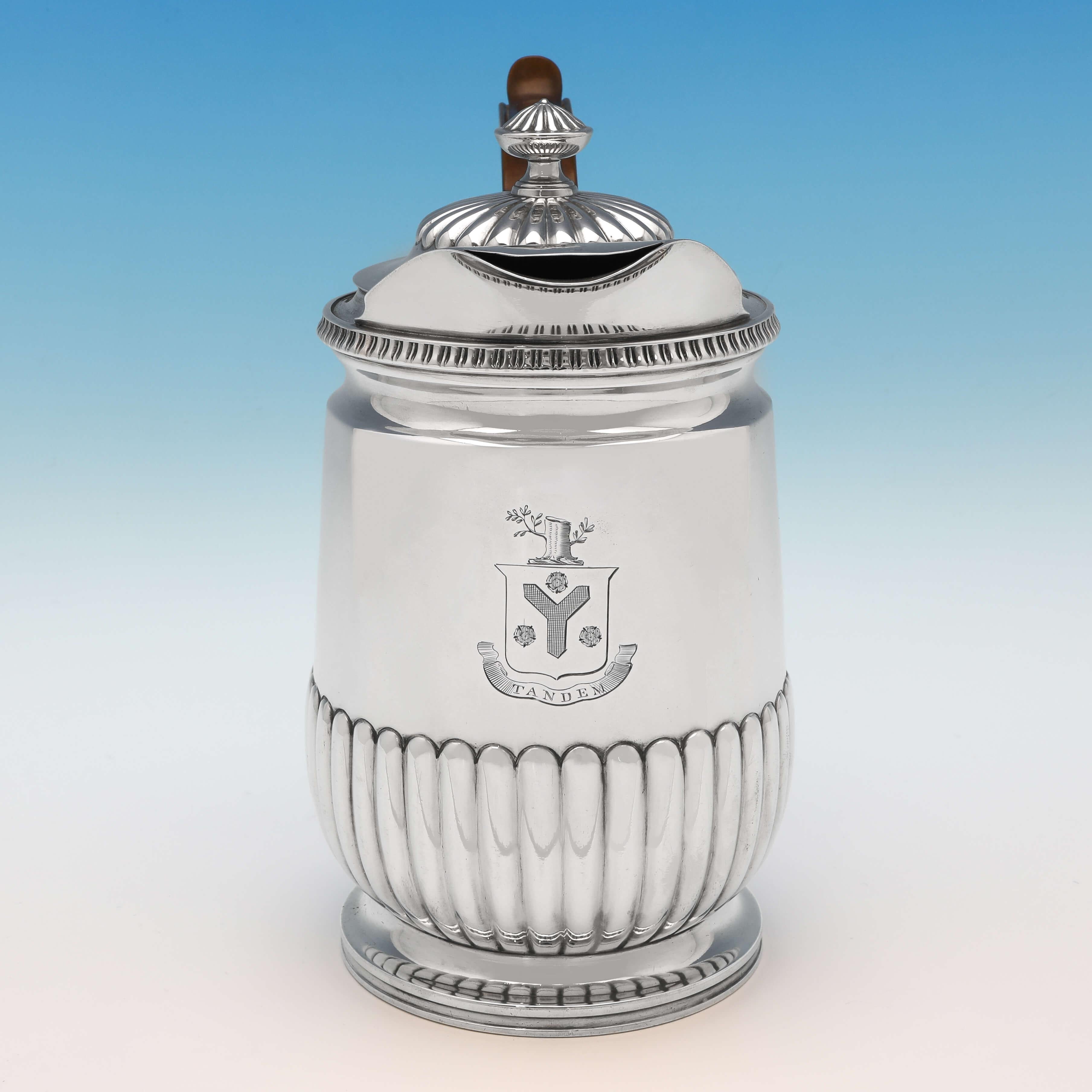Hallmarked in Birmingham in 1811 by Matthew Boulton, this handsome, Regency period, antique sterling silver water jug, features half fluted decoration to the body and lid, an egg and dart border, a wooden handle, and an engraved crest and motto to