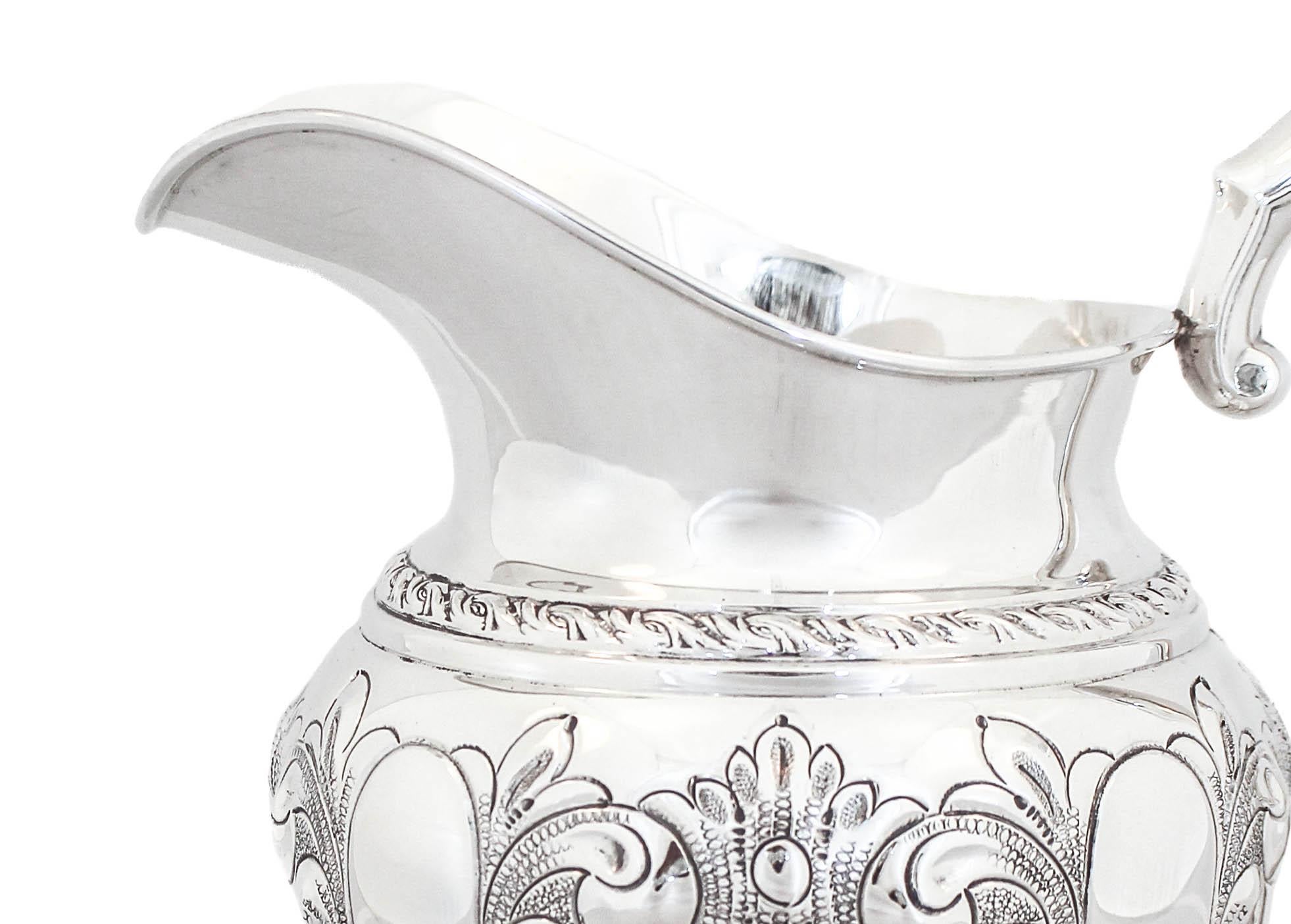Being offered is a sterling silver water pitcher by Amston Silver Company of Meriden Connecticut.  It is hand-chased (signed hand-chased) with flowers, leaves and paisleys all around the body.  There is a gadroon around the base as well as the neck.