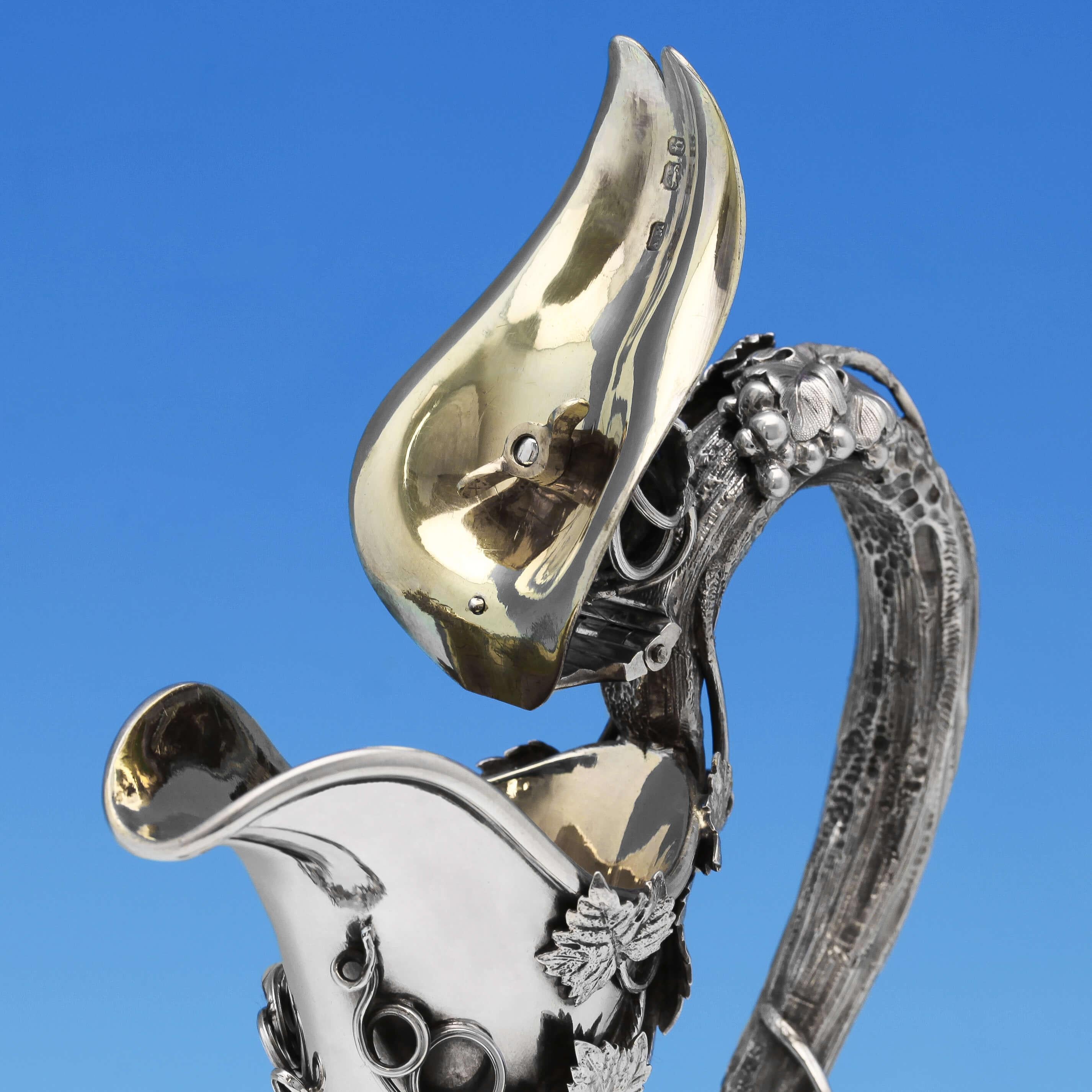 Hallmarked in London in 1857 by Alexander Macrae, this classical Victorian, antique, sterling silver wine ewer, features cast and applied grape and vine decoration, a plain body, and a vine handle. The wine ewer measures: 13.5