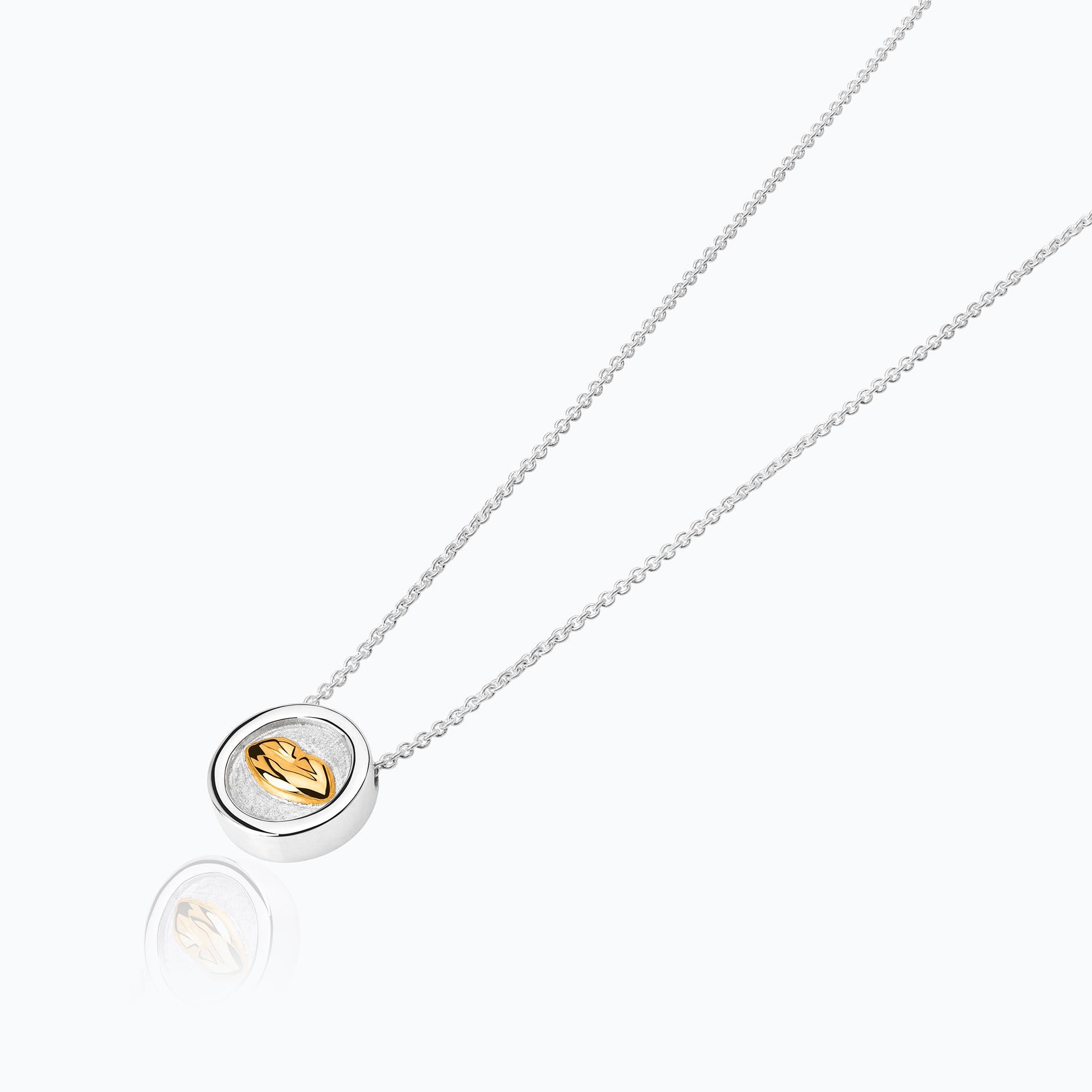 The Bésame Medal Vermeil Pendant from the Bésame collection by TANE is made in sterling silver with 23 karat yellow gold vermeil. In the center of the medal, the collection's insignia kiss emerges in relief, framed by a polished silver bezel, the