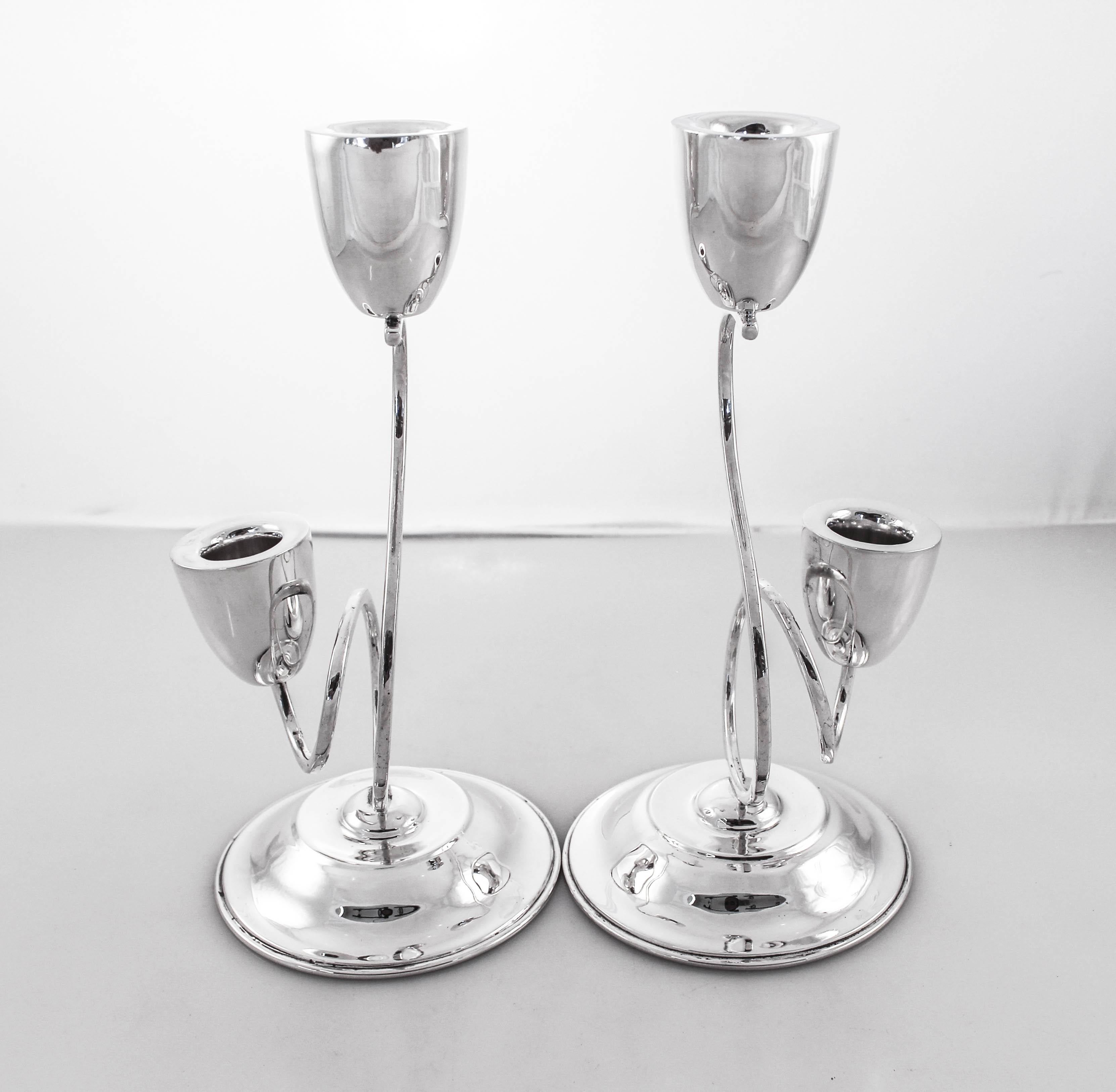 A pair of sterling silver two-branch candelabras from 1952. The taller candleholder stands at 10 inches while the other is 4.5 inches high. They are connected with a curled S-shaped piece, giving these candelabra a more casual midcentury feel. The