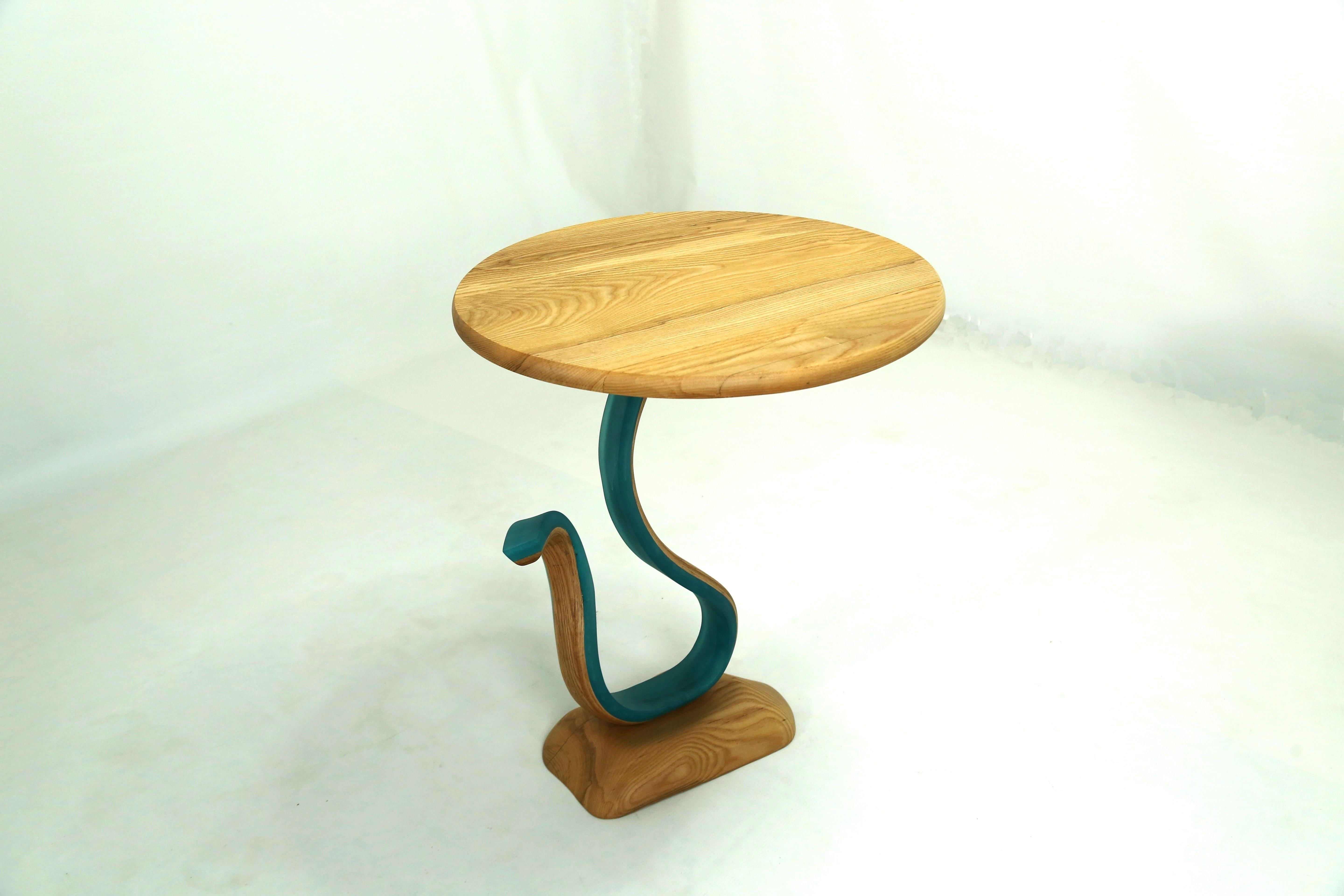 Der Sterope Table ist ein Beistelltisch mit einer runden Eschenholzplatte und einem frei geformten Sockel. Der Körper des Stücks besteht aus Harz, das mit Eschenholzstreifen verschmolzen ist, die sich zusammen drehen und wenden und dem Stück seine