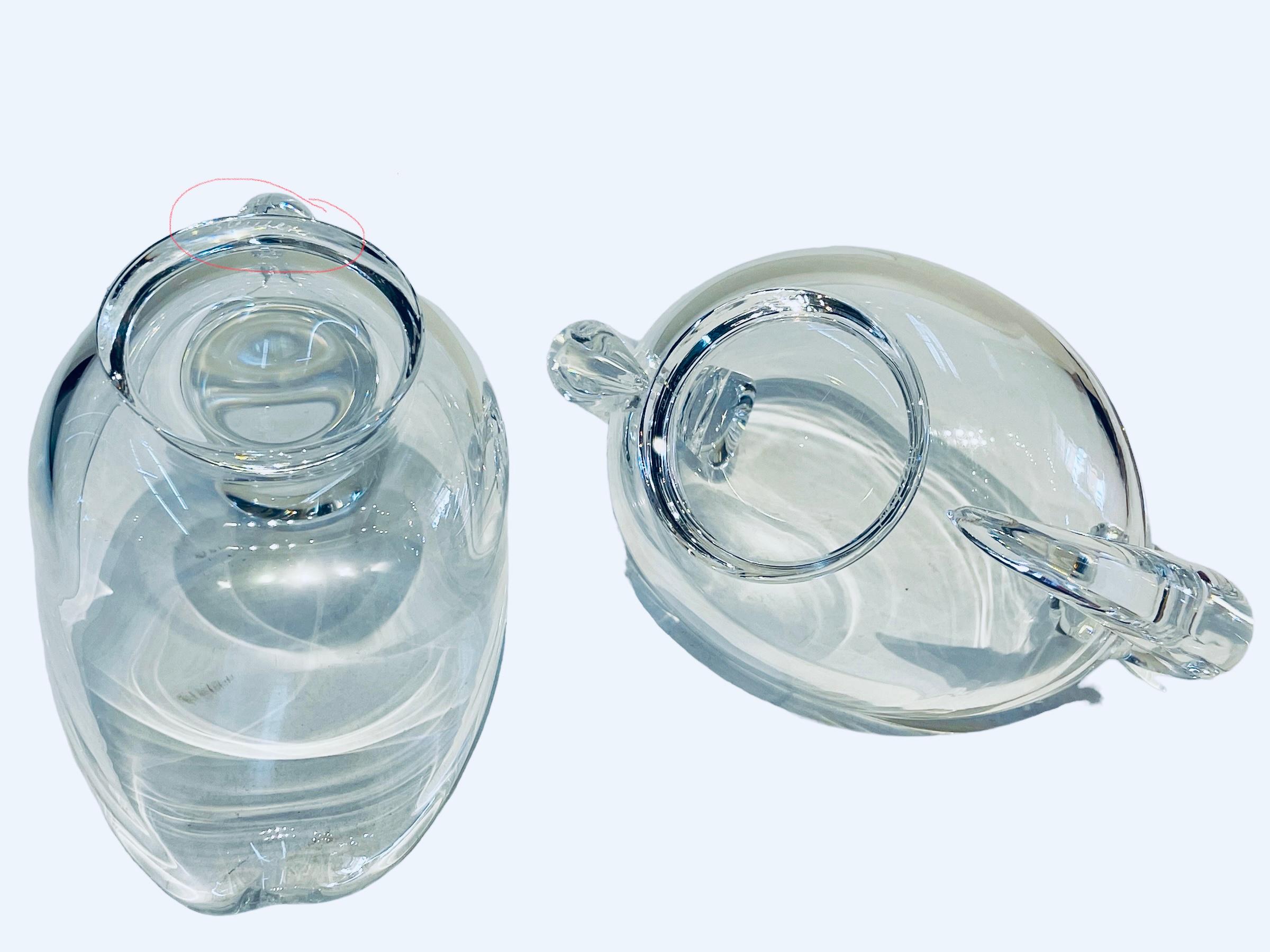 Questo è un set di lattiere e zuccheriere Steuben Glass. Raffigura una ciotola in vetro trasparente di forma ovale con manici a volute di lumaca. Sotto la base rotonda c'è il marchio di Steuben inciso con acido.