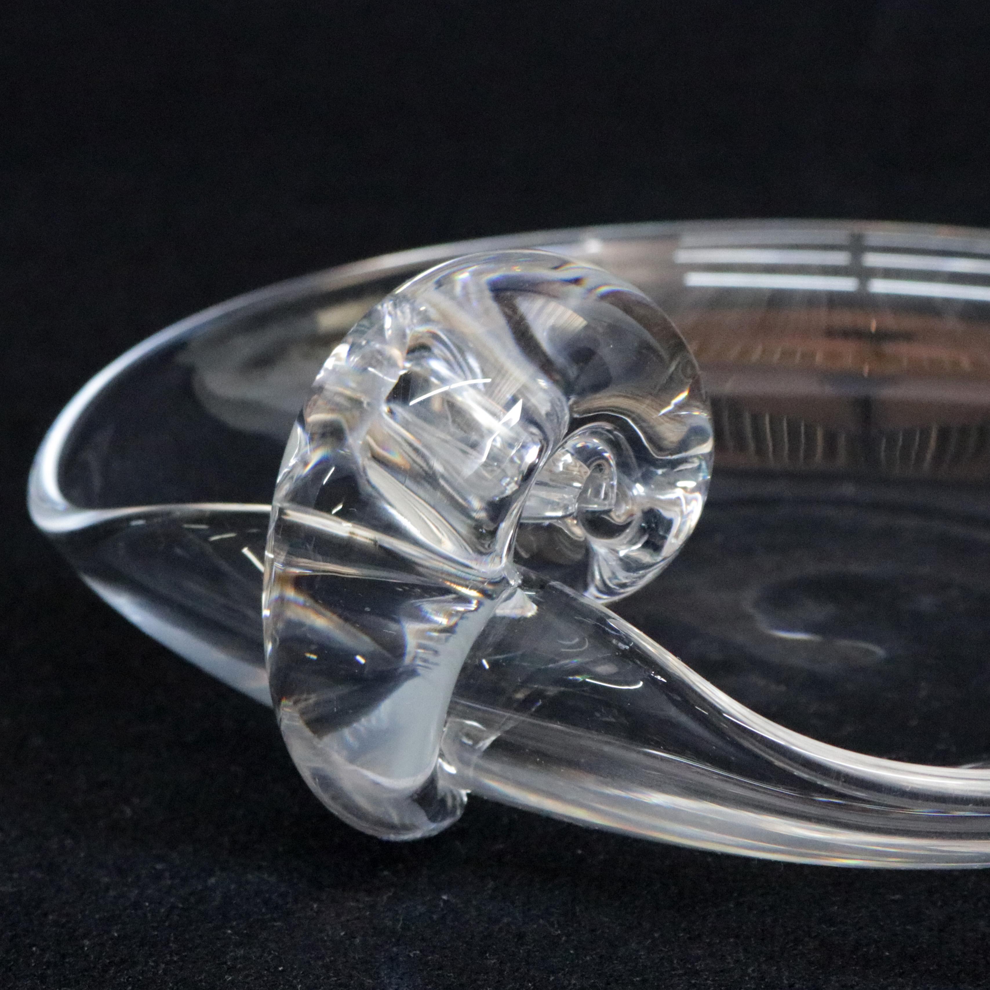 A midcentury Steuben mouth blown crystal candy dish feature colorless art glass with sloping bowl and classic scrolled nautilus form handle designed in the 1940s for Corning Museum of Glass, New York, NY, signed on bases, 20th century.

Measure: