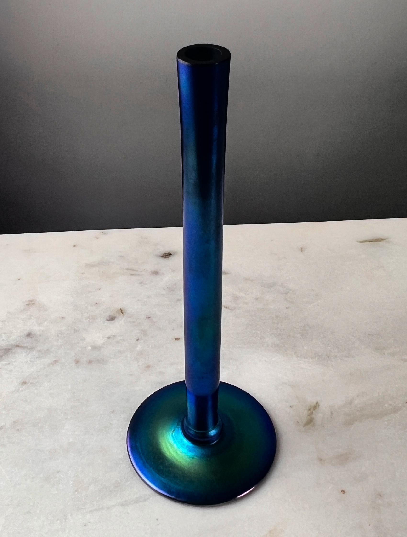 Cet exquis vase à bourgeons bleu auréolé de Steuben Glass Works, style #2556, a été fabriqué à l'époque remarquable de Frederick Carder, entre 1903 et 1932. Réputée pour son étonnante finition irisée, cette pièce incarne les principes du mouvement