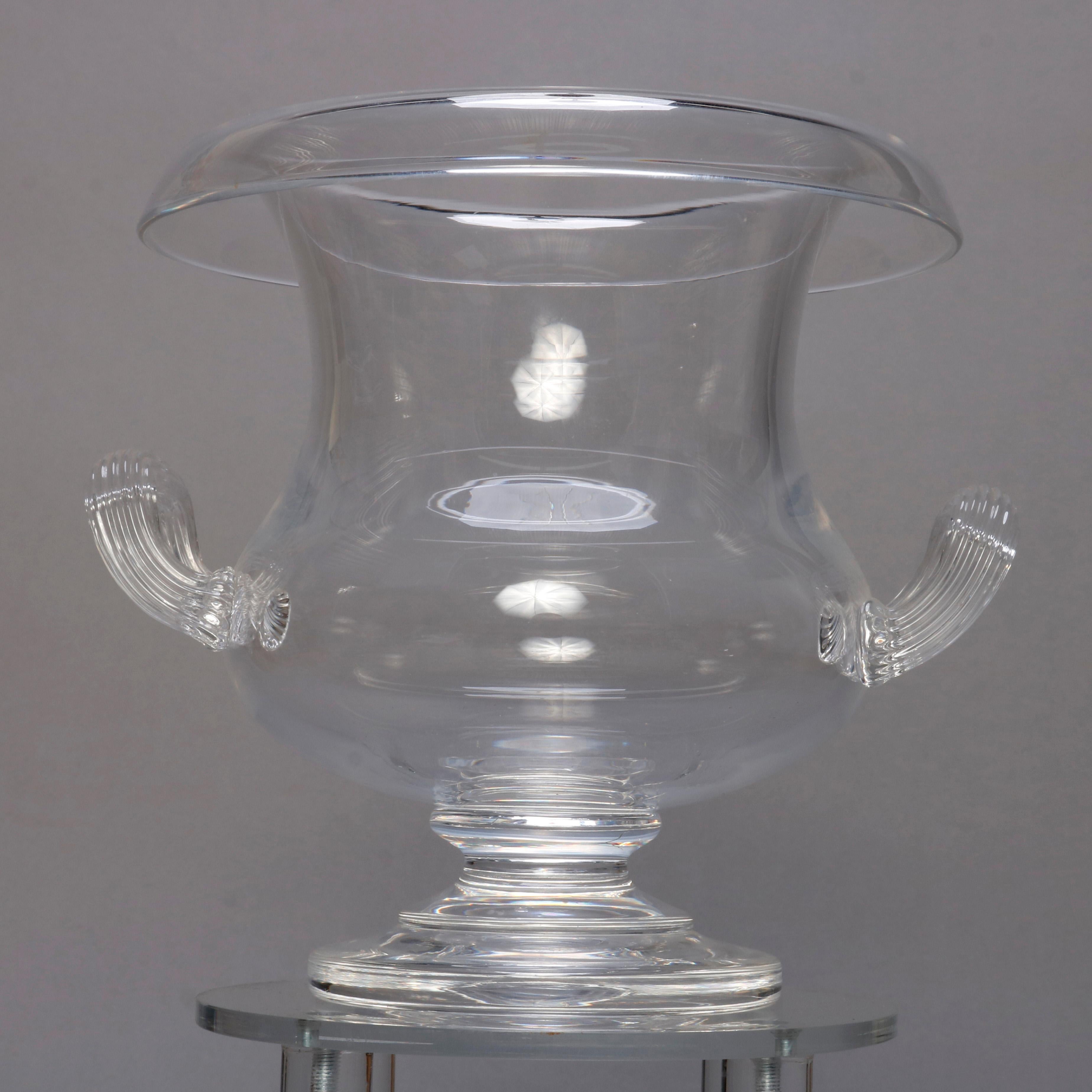 A crystal center bowl by Steuben Glass Works offers urn form with rolled rim, double ribbed applied handles and raised on central plinth, signed on base as photographed, 20th century

Measures: 7.25