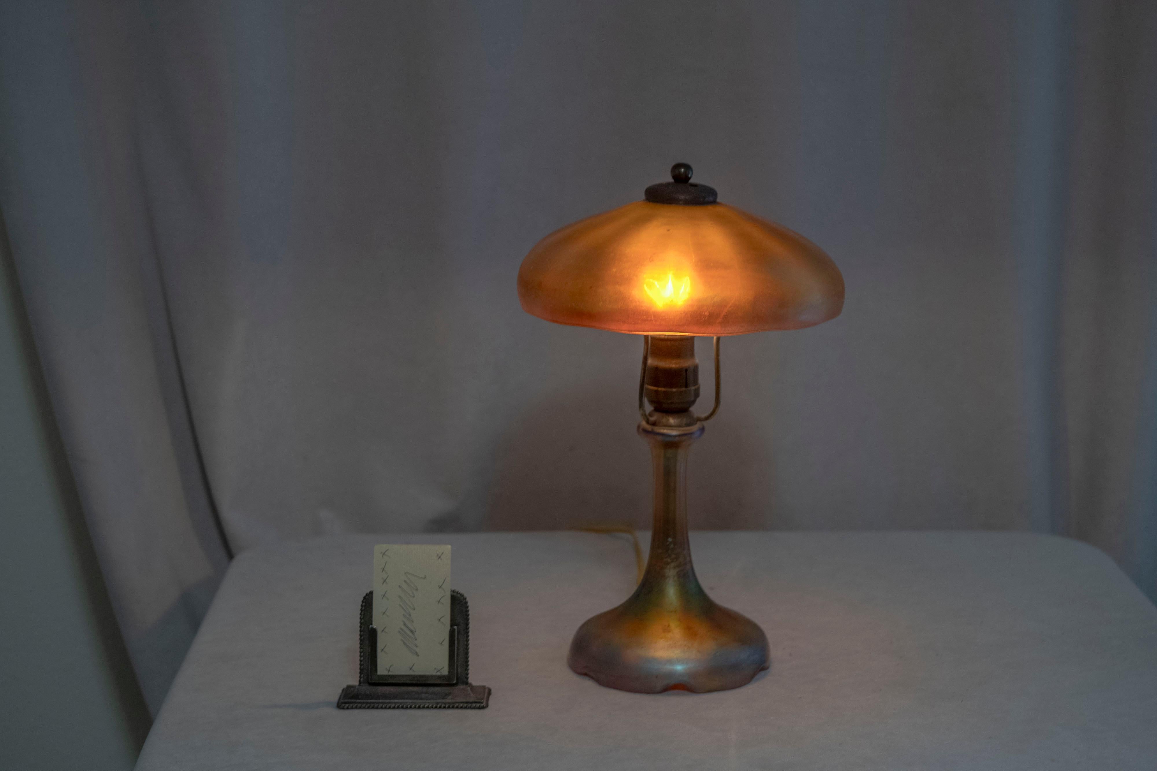  This warm and high quality lamp was done by Steuben Glass. While not signed we believe it was their work. Every part is original, from the heat cap, finial, shade and base. Very hard to find these lamps with a glass base intact as well as the shade
