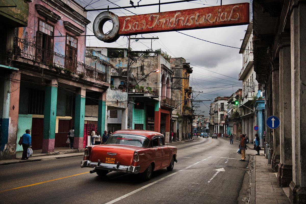 Steve McCurry Color Photograph - A red car driving through the streets of Havana, Cuba
