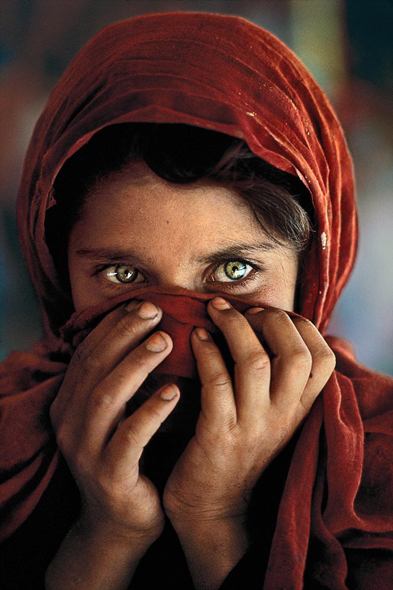 Afghan Girl with Hands on Face by Steve McCurry presents a powerful portrait. A young girl with piercing green eyes stares off in the distance. She wears a red scarf around her head and holds it up to her face. 

Afghan Girl with Hands on Face by