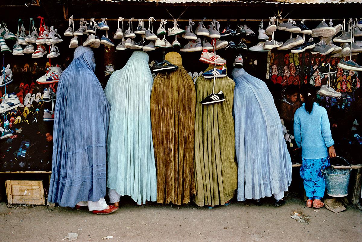 Afghan Women at Shoe Store, Kabul by Steve McCurry is a 20 x 24 inch digital C-Print, printed on FujiFlex Crystal Archive Supergloss Paper. This photograph features 5 Afghan women at a market, looking at a stand of shoes. The photograph is signed by