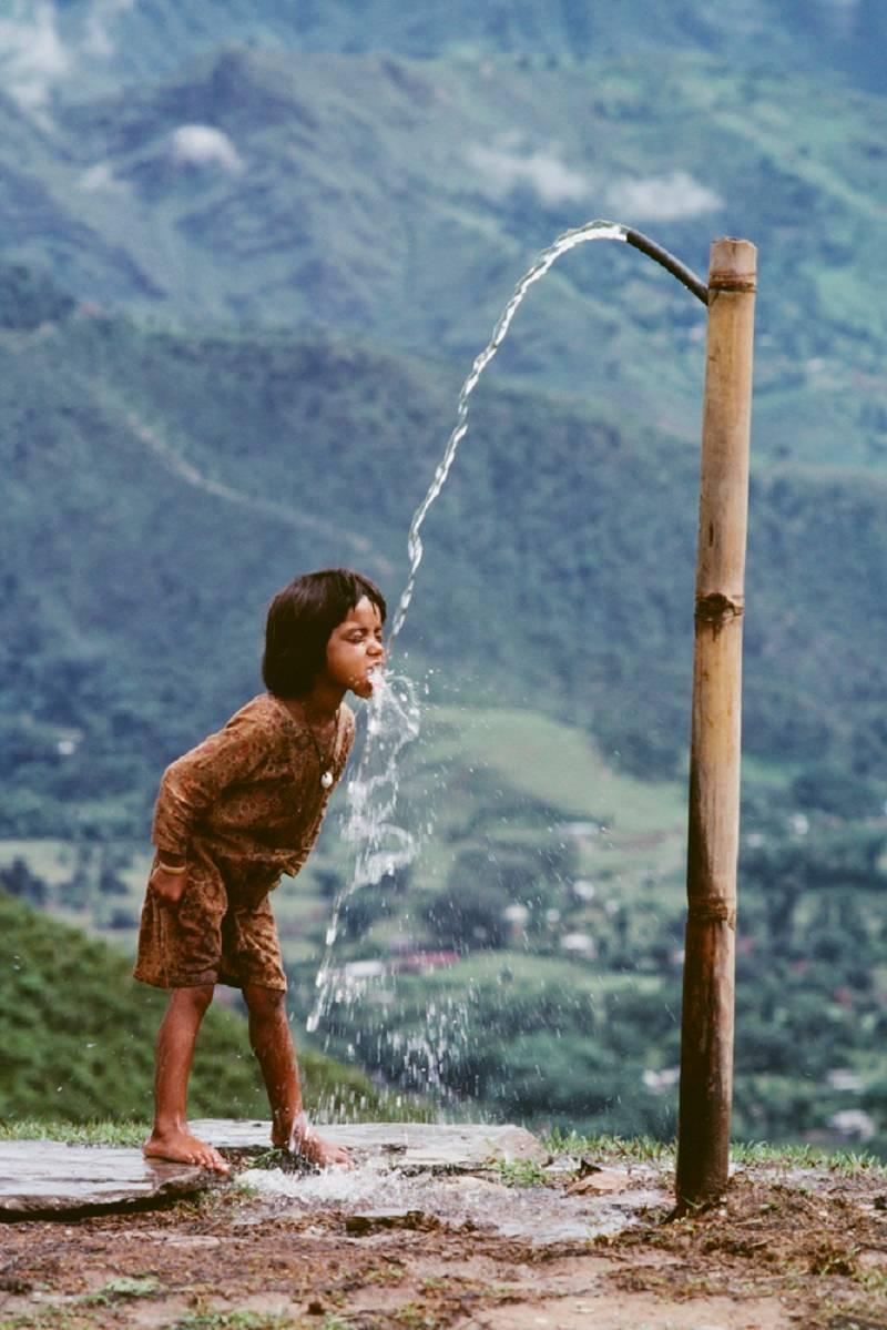 Steve McCurry Color Photograph - Child Drinks Water from Well, Nepal