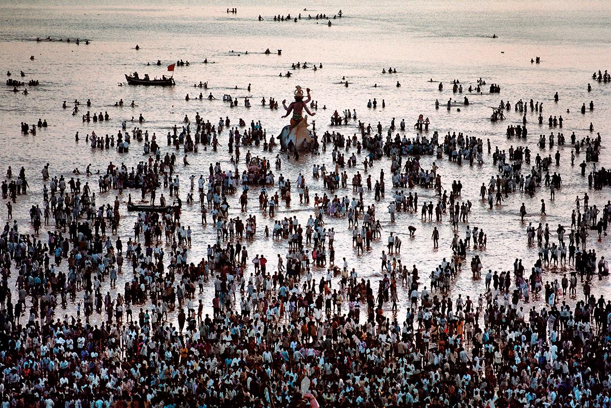 Ganesh Chaturthi Festival von Steve McCurry zeigt eine Menschenmenge, die im Rahmen ihrer Feierlichkeiten in das seichte Wasser des Meeres geht. Die Menschen versammeln sich um eine große Statue des Hindu-Gottes Ganesha, während sie weiter in