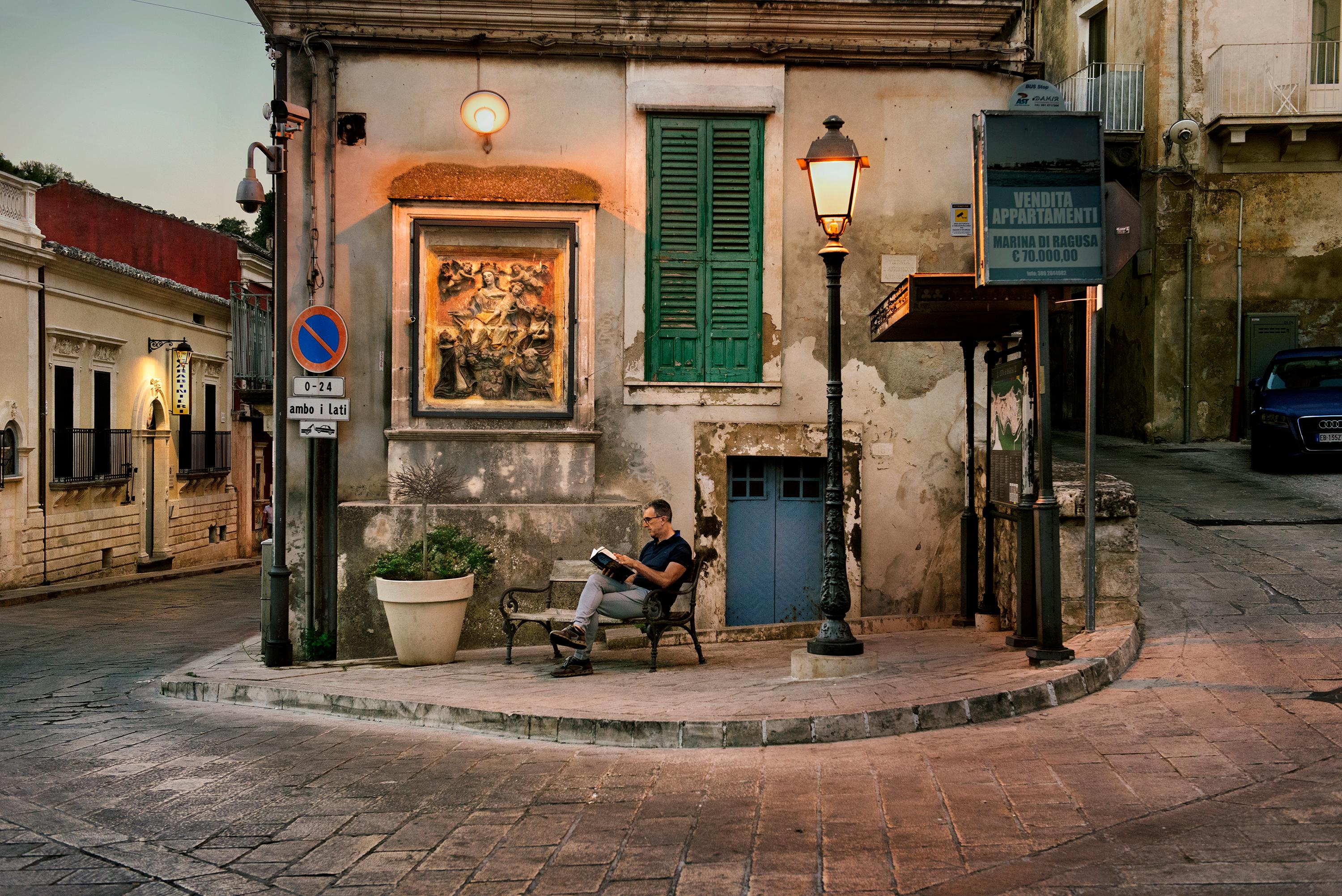 Steve McCurry Color Photograph - Man Reads on Sidewalk