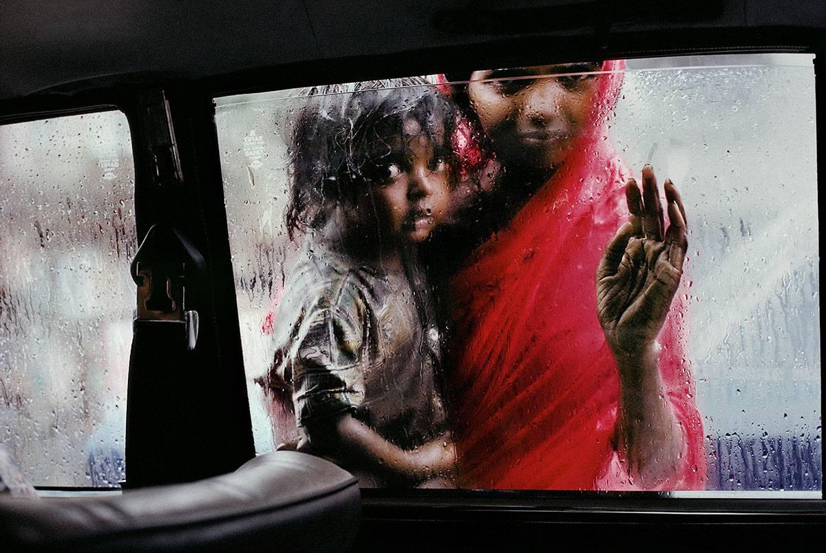 Steve McCurry Landscape Photograph - Mother and child looking in through a taxi window, Bombay, India