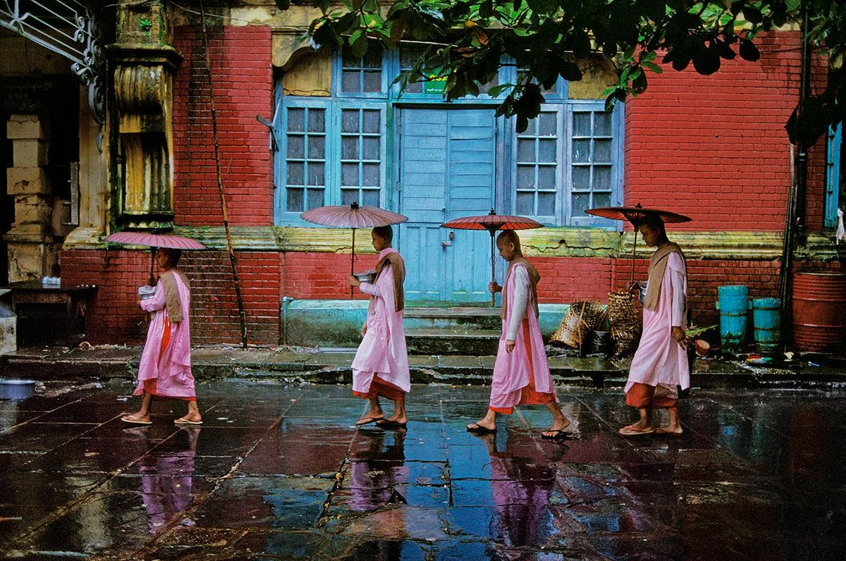 Procession of Nuns by Steve McCurry is a 20 x 24 inch digital c-print on FujiFlex Crystal Archive Supergloss Paper, available in an edition of 90. This photograph features four nuns, dressed in pink robes and holding flat umbrellas, walking in front
