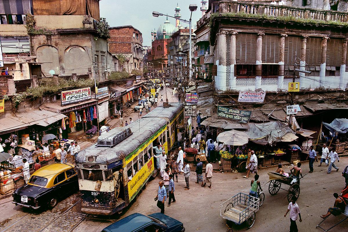 Tram, Calcutta by Steve McCurry depicts a bustling intersection. The streets are lined with markets selling fruit, clothes and other varying products. People fill the streets, some walking or biking, adding lively energy into this cityscape.

Tram,