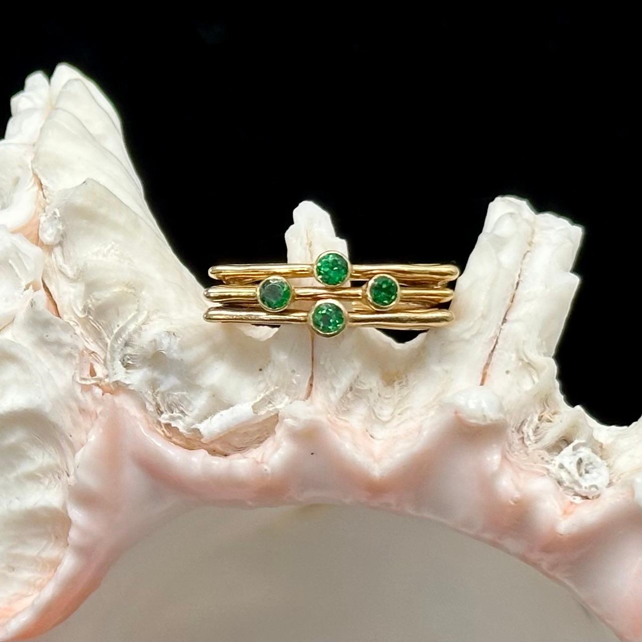 Three separate, interestingly sculpted spiral ornamented rings create a geometric  pattern of brilliant electric green with an arraignment of 3 mm round faceted tsavorite garnets in the center.  The 3 flat lines of gold with the central stones