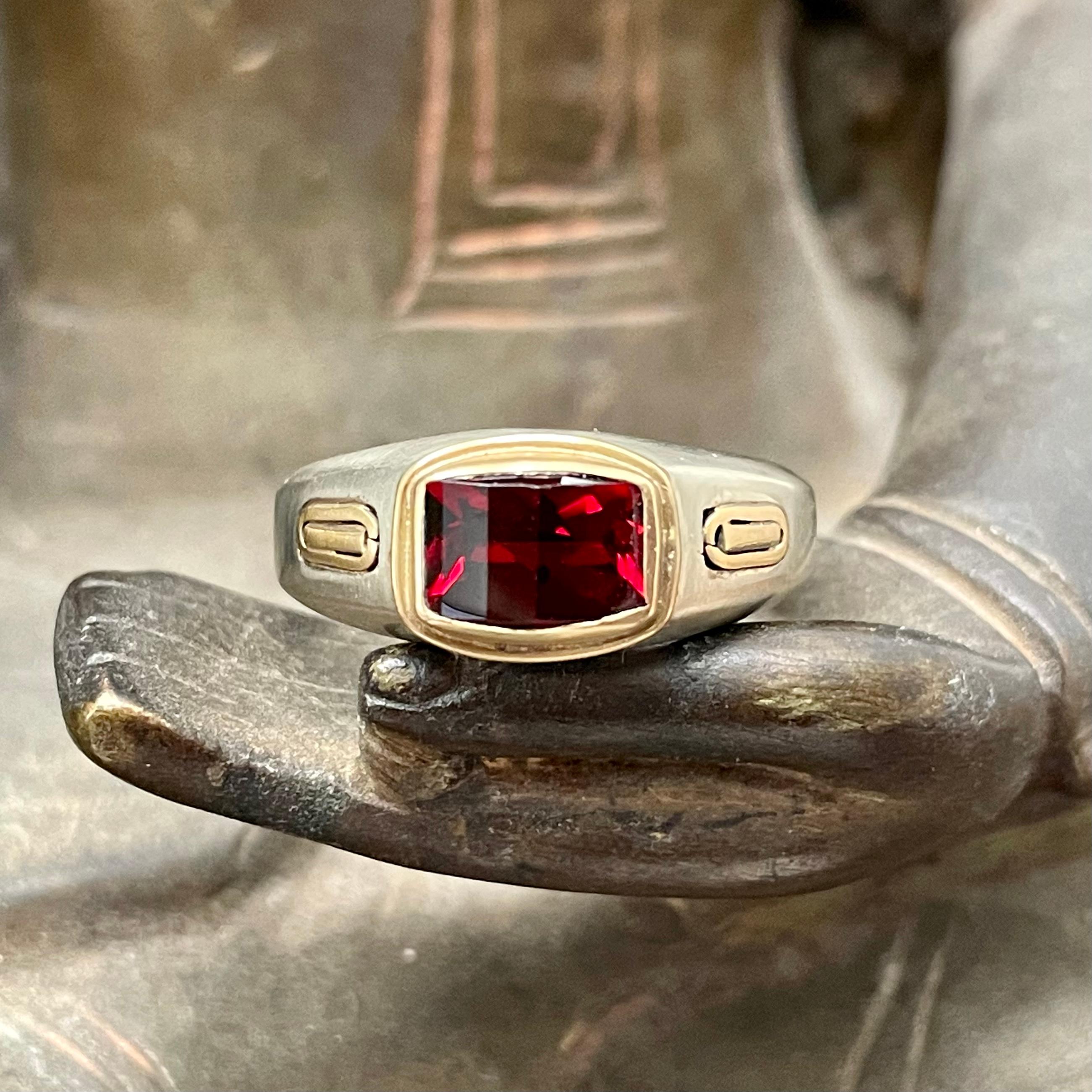 An interesting barrel-cut 6 x 8 mm Mozambique garnet is set within an 18K yellow gold mount with side accent 18K yellow gold bars in a somewhat flat tapered matte-finish 14K white gold shank in this design.  A clean and nicely balanced modern look.