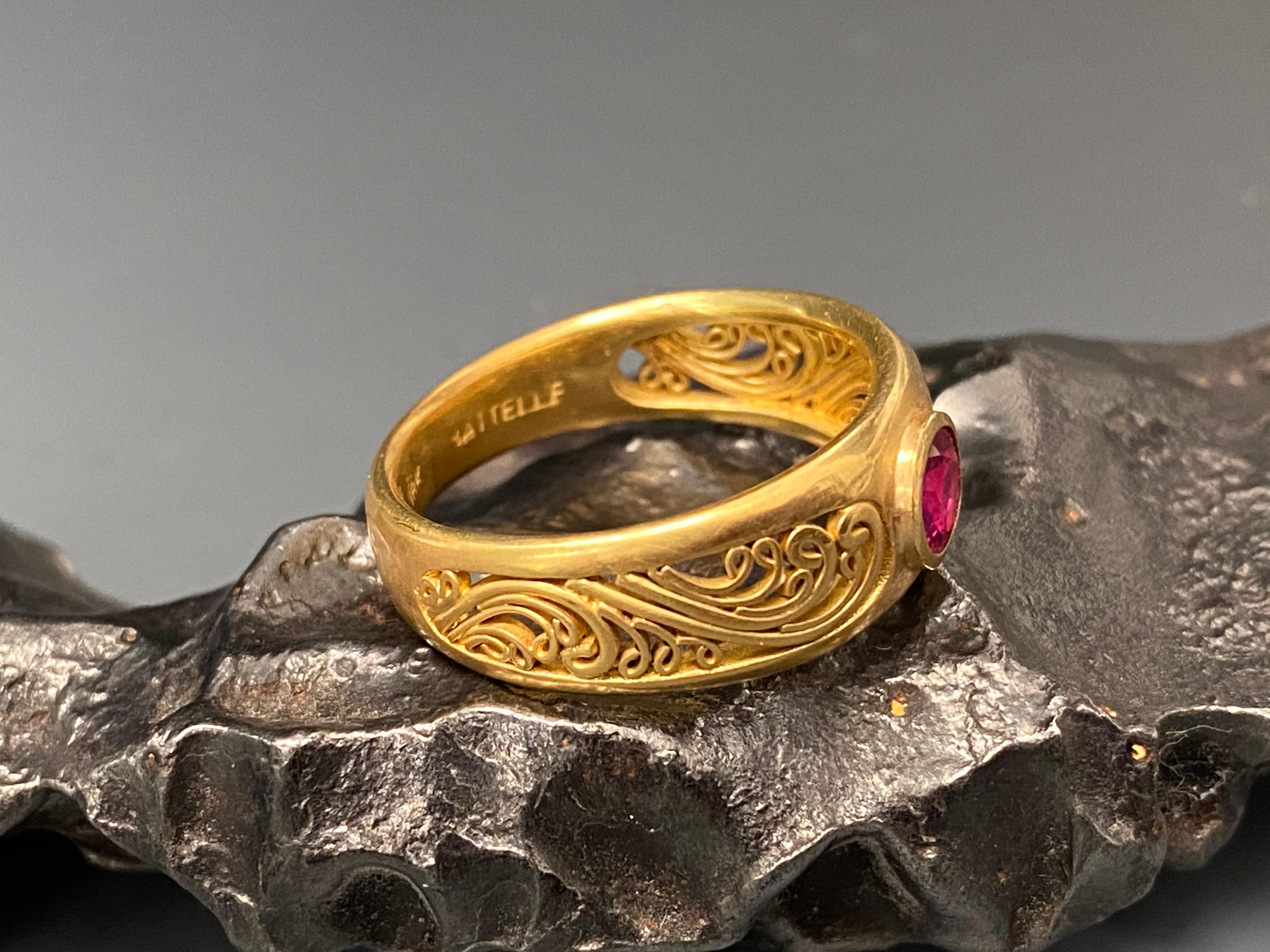 A substantial and comfortable gapped 18K gold shank is inset with fine handset scroll wire work on both sides of its central 5mm round faceted pink Thailand ruby in this design.  A nice juxtaposition stone and motif.  This ring is currently sized 7.