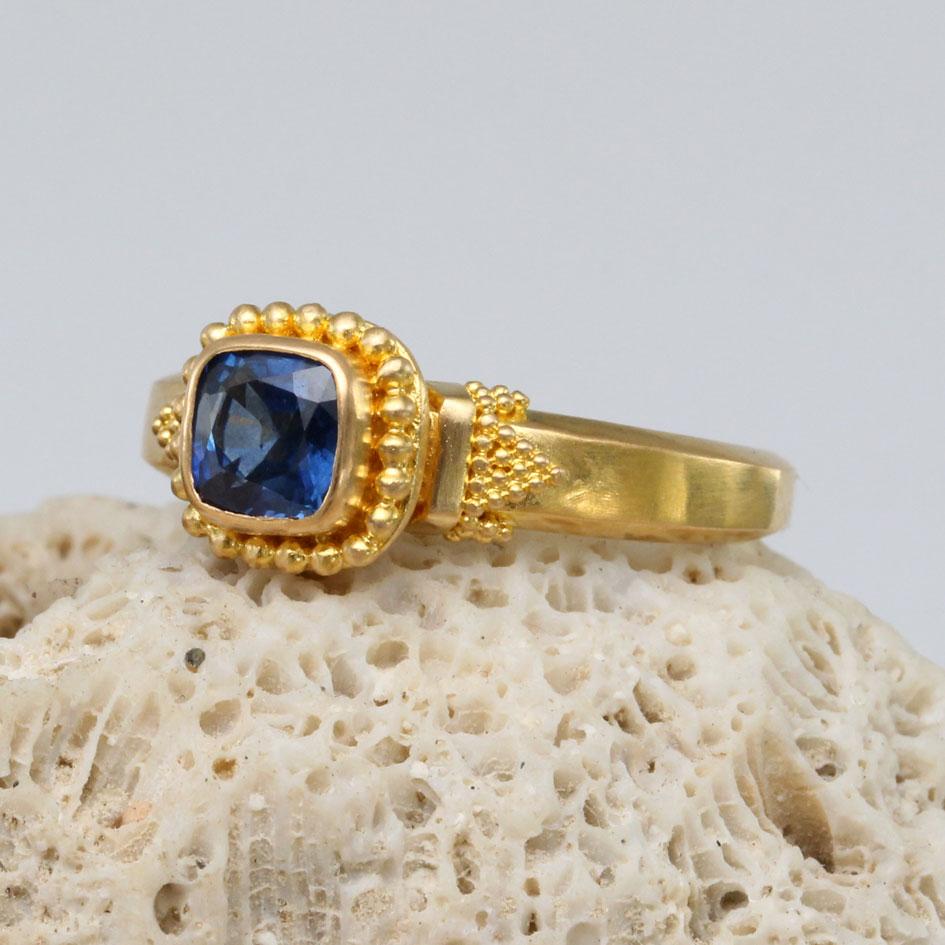A top grade 5 mm cushion cut blue sapphire is highlighted by large and small surrounding 