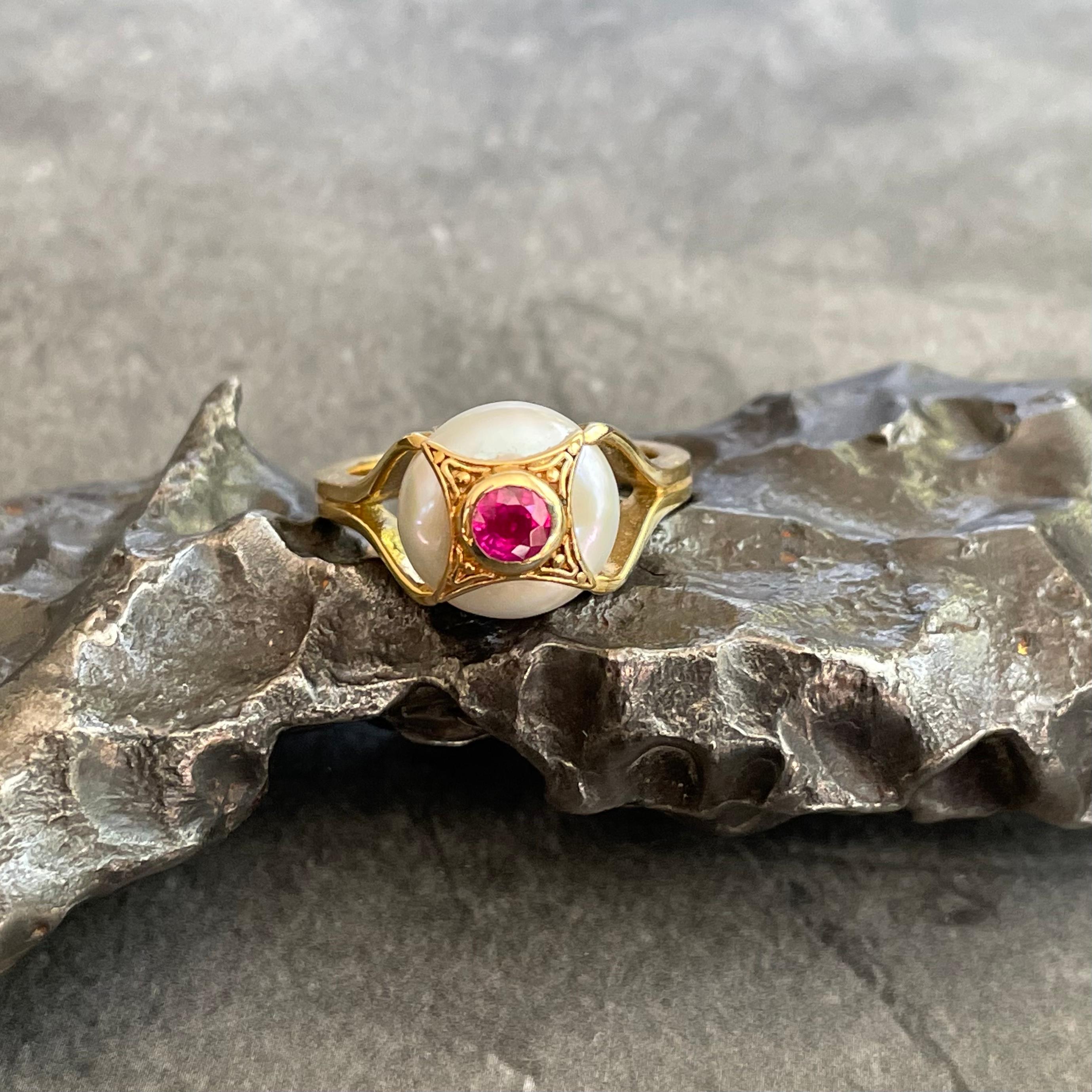 A combination of a white button pearl inset with a 4 mm faceted ruby and handmade wirework and granulation atop a split 18K shank is truly a one-of-a kind design showing the colors of white, gold, and ruby pink. This ring is currently sized 7. It is