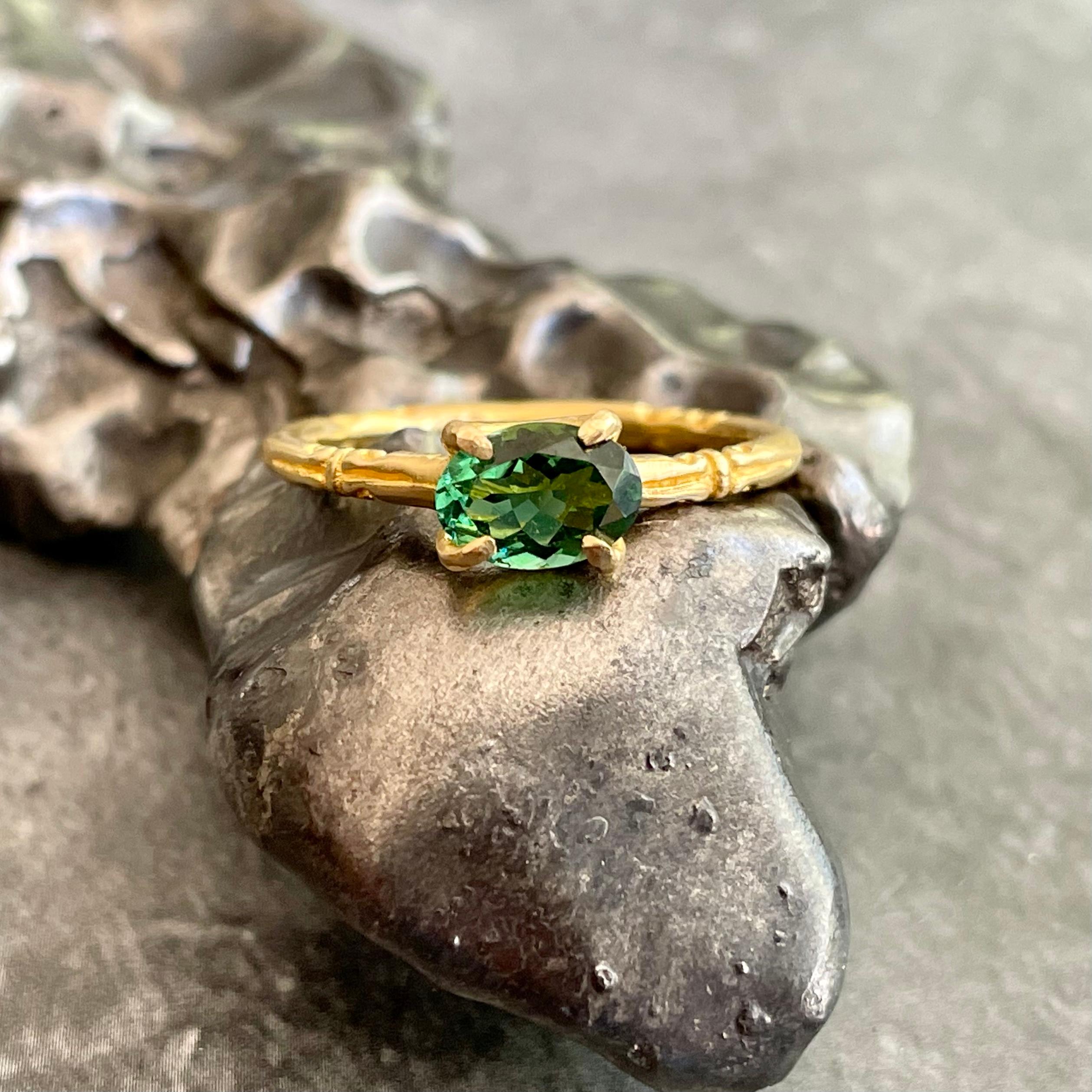 A sparkling 5 x 7 mm oval faceted green tourmaline is held in 4 prong embrace atop an interesting  Steve Battelle designed 4 opposing spirals ancient-inspired round shank.  This ring is currently sized 6.5.  It is easily resizable. 