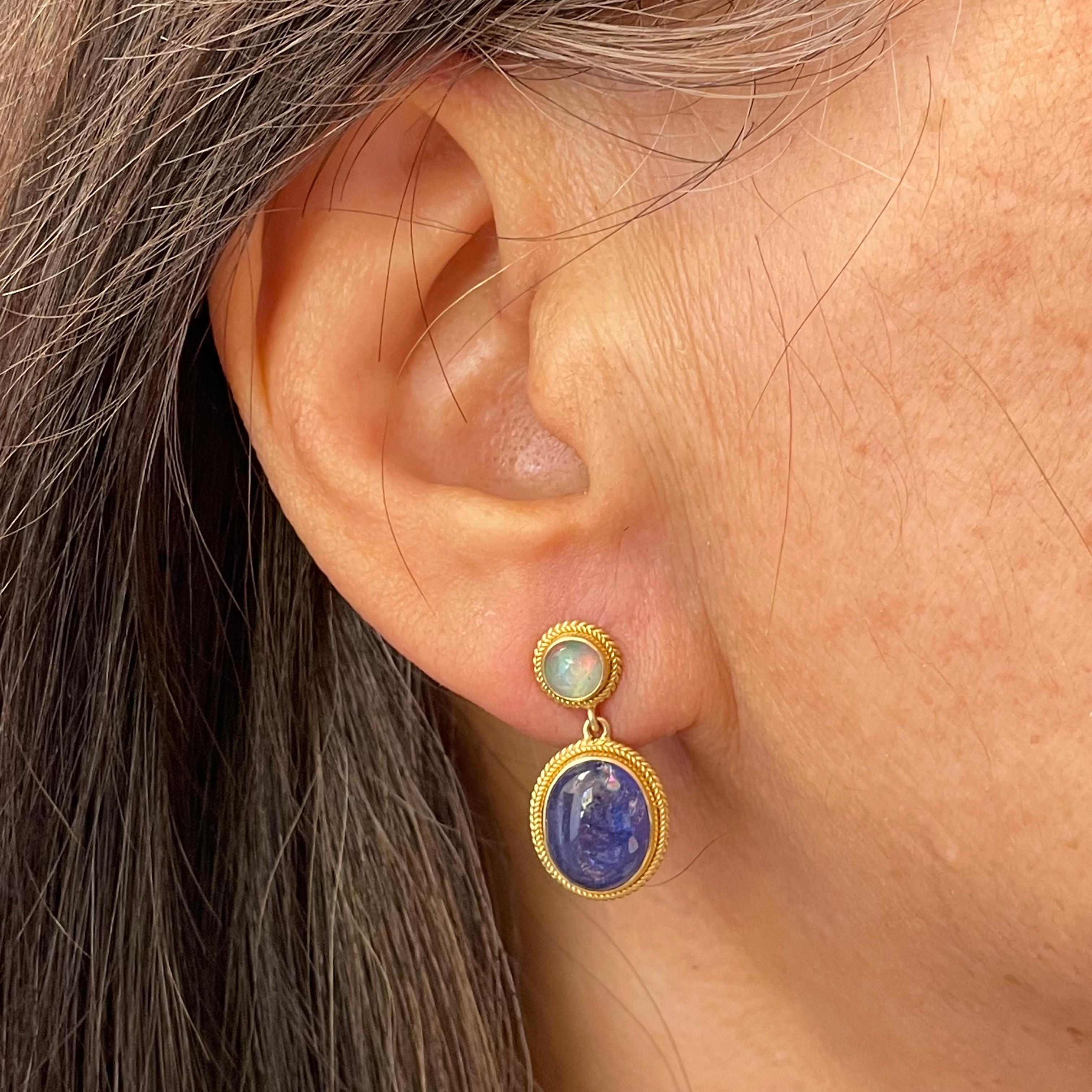 Complementary deep blue 9 x 11 mm tanzanite cabochons are paired with fiery greenish and reddish Ethiopian opal 5mm rounds in this Steven Battelle design.  The stones are surrounded by rich double-braided wire settings to enhance.  
