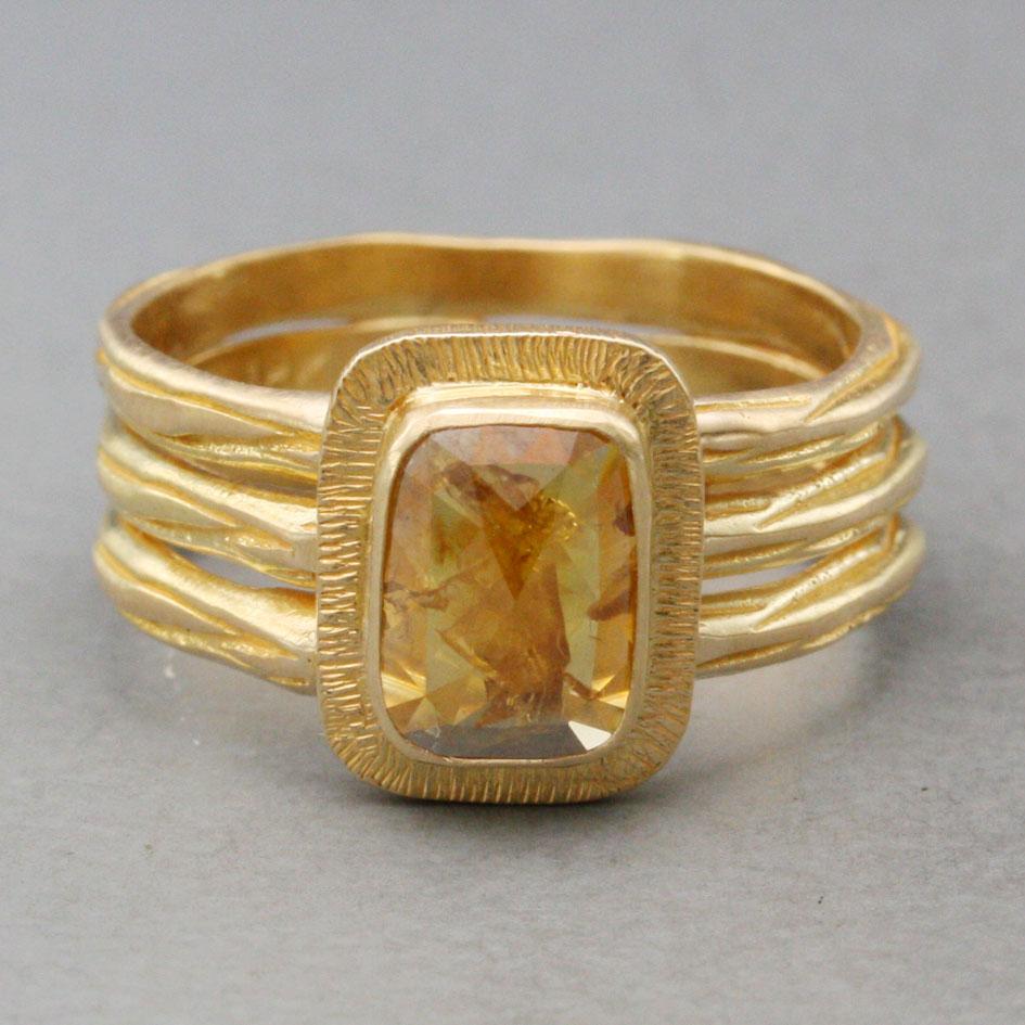 A lustrous, variegated 6 x 8 mm cushion shaped rose-cut yellow diamond is set vertically surrounded by a 
